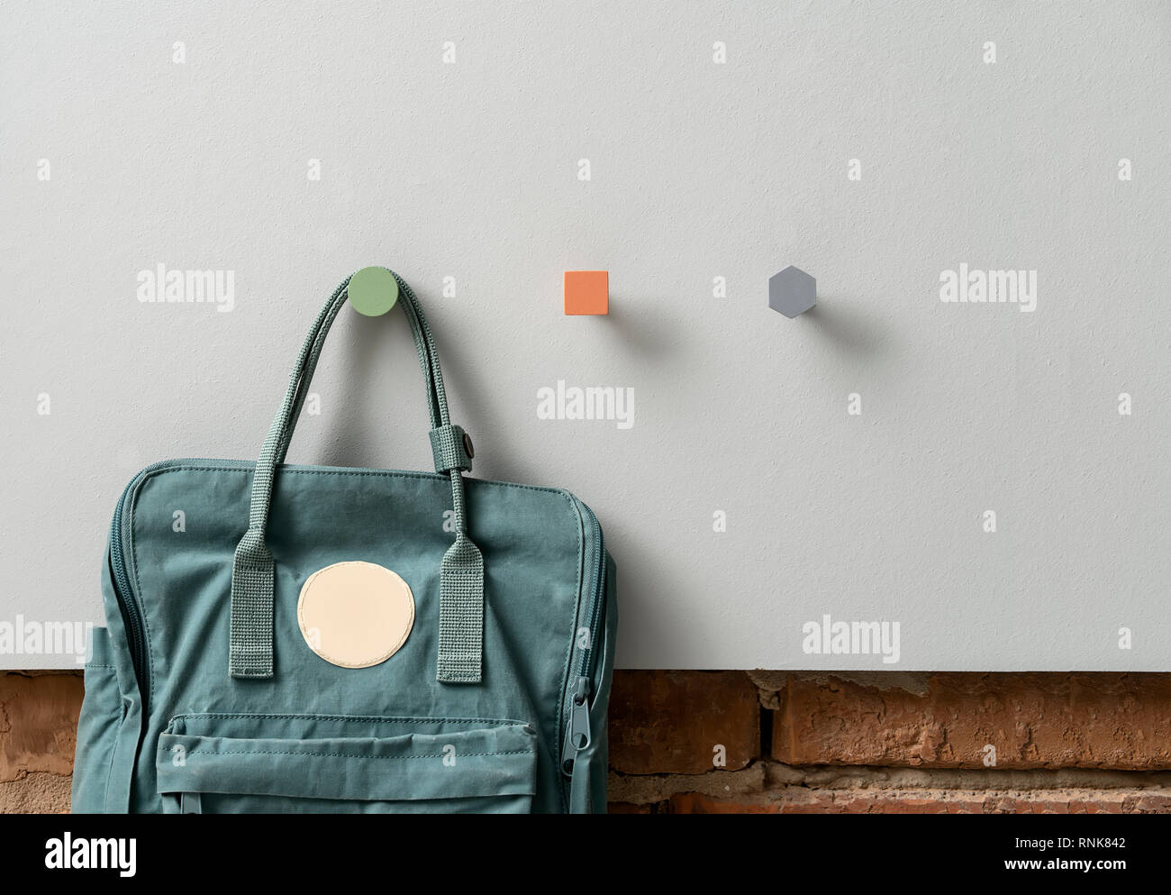 Teal backpack is hanging on the metal green round hanger on the textured  gray panel on the brick wall background indoors. Next to it there are  orange Stock Photo - Alamy