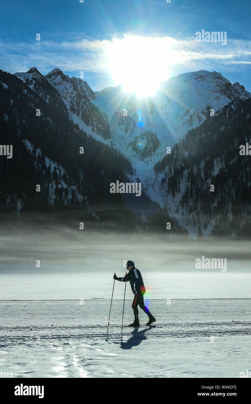 Anterselva lake, Pusteria valley, South Tyrol, Italy - February 16, 2019:  A woman skies on the Anterselva frozen lake as the early morning sun appear Stock Photo