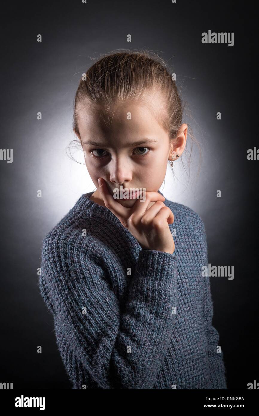 Teen girl 9-12 years old, looks into the frame, emotional studio portrait on a gray background with backlight Stock Photo