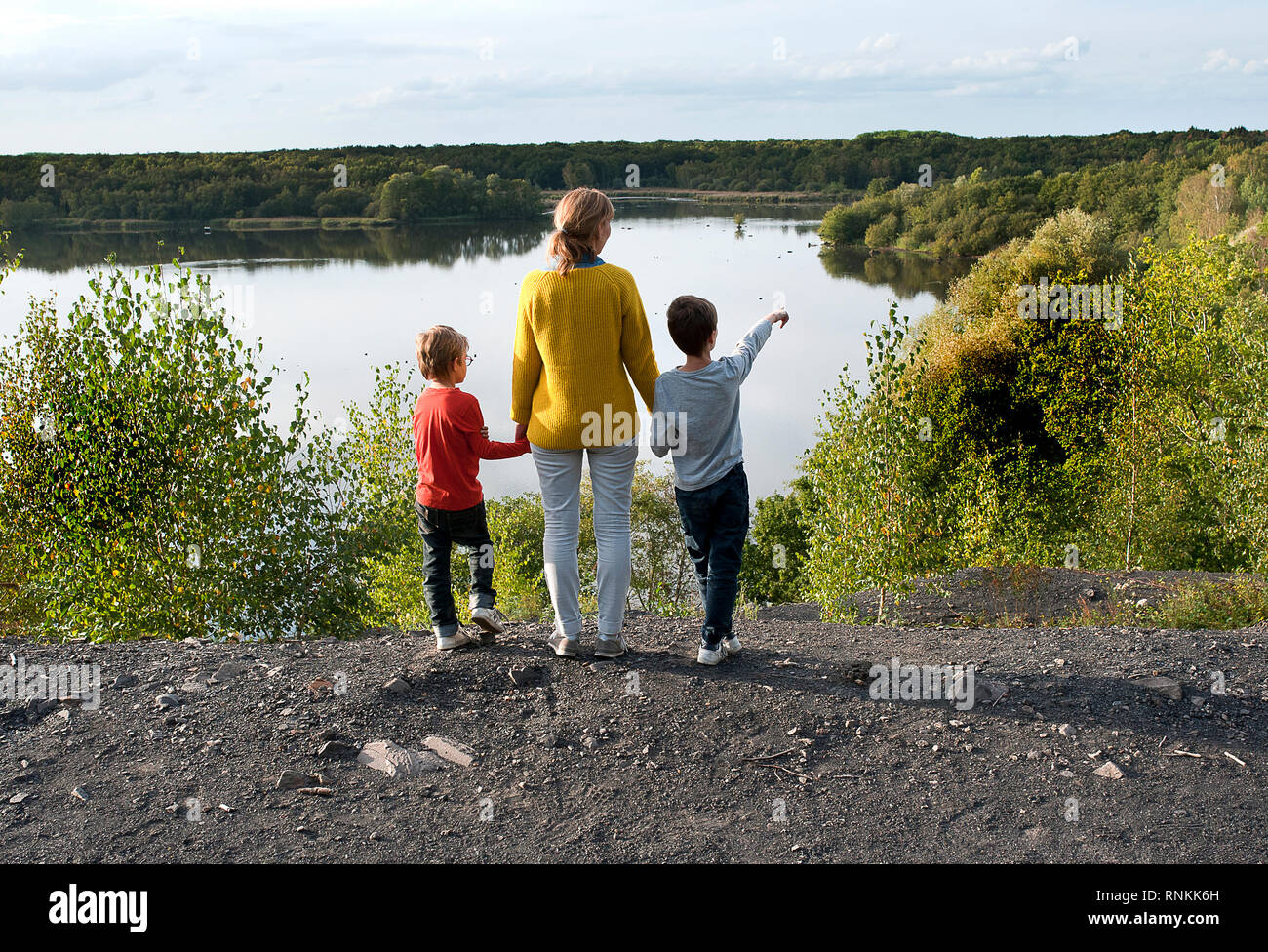 Woman, mother with her two children, holding hands, facing the lake ' Lac de la mare ' in Goriaux, in the forest of Raismes-Saint Amand Wallers, Scarp Stock Photo