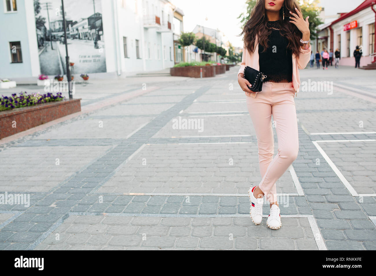Stylish girl in pink sport chic suit, lace top and sneakers posing in the  street with small crossbody bag in hand Stock Photo - Alamy