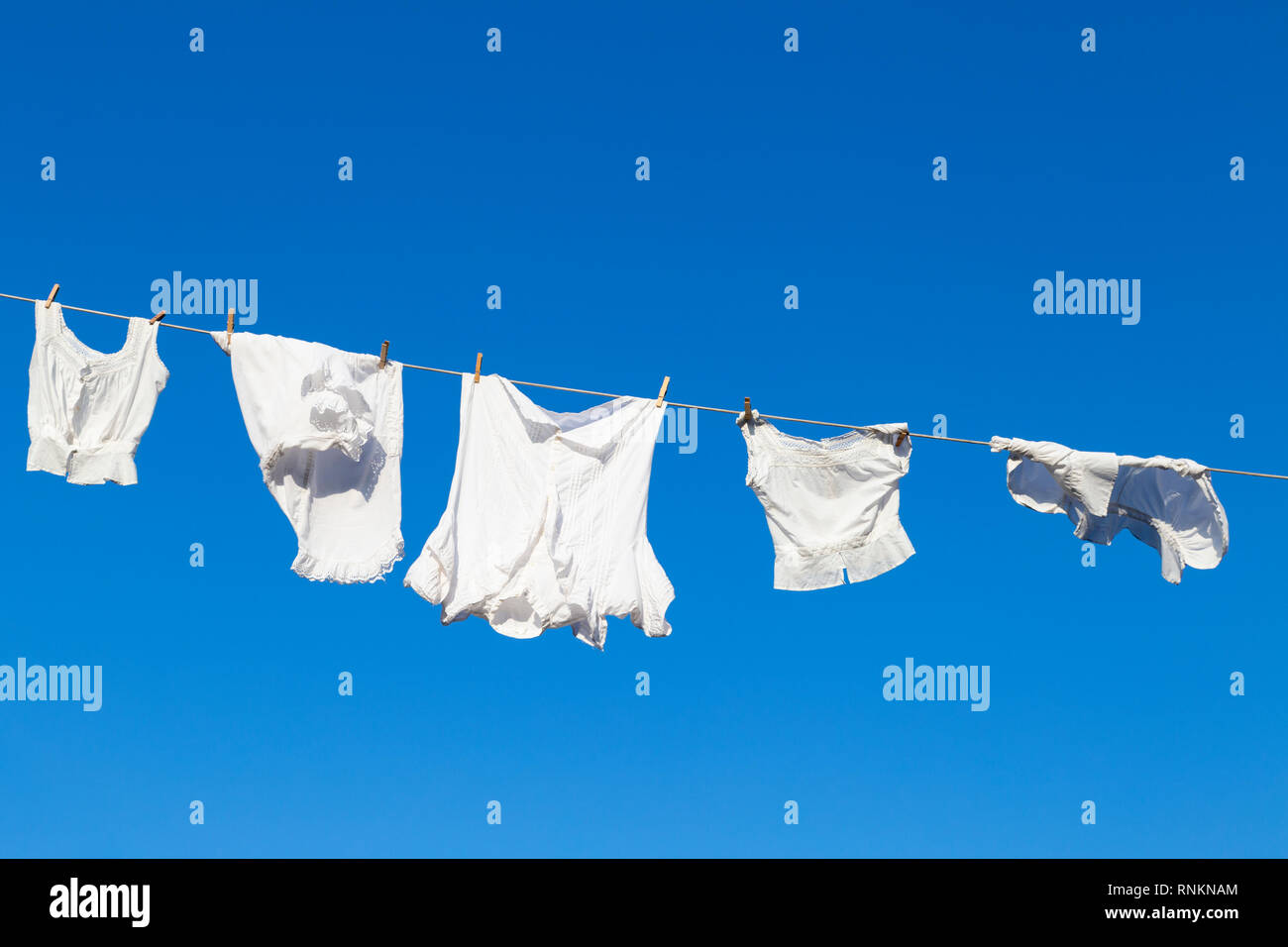 Clean white laundry hanging to dry on a rope against the blue sky during a beautiful sunny day Stock Photo