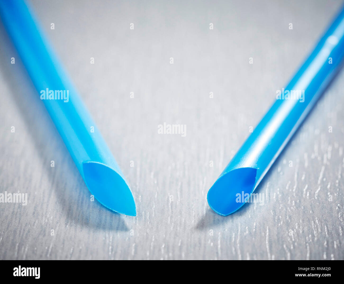 Two blue plastic drinking straws on gray background. Studio Picture Stock Photo