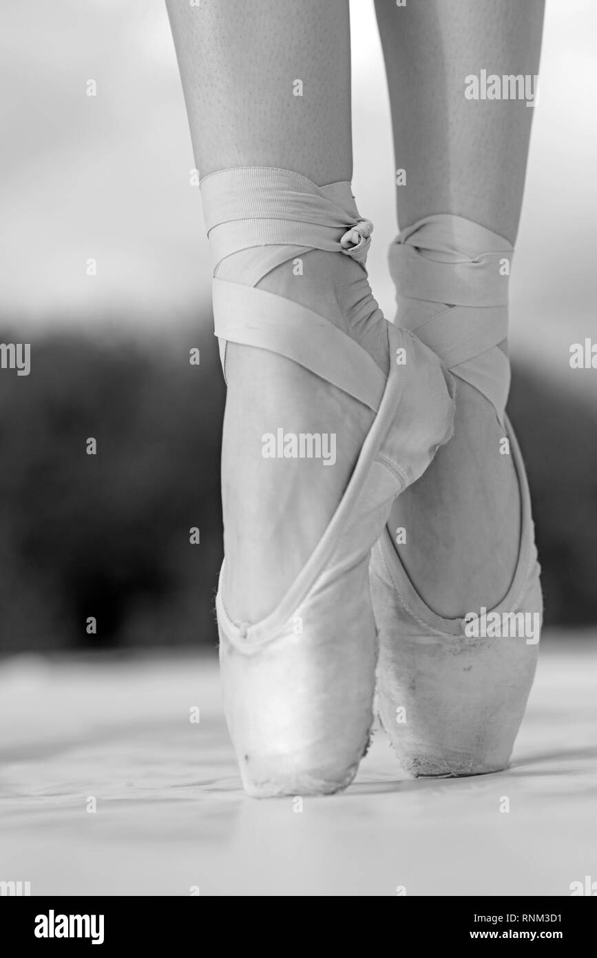 On the tips of the toes. Female feet in pointe shoes. Pointe shoes worn by ballet dancer. Ballerina shoes. Legs in white ballet shoes. Ballet slippers Stock Photo