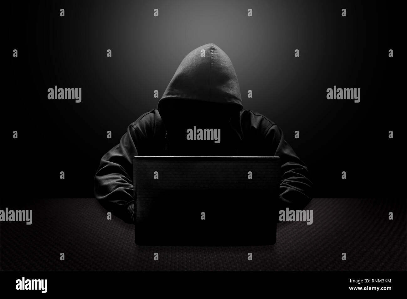Hooded computer hacker stealing information with laptop Stock Photo
