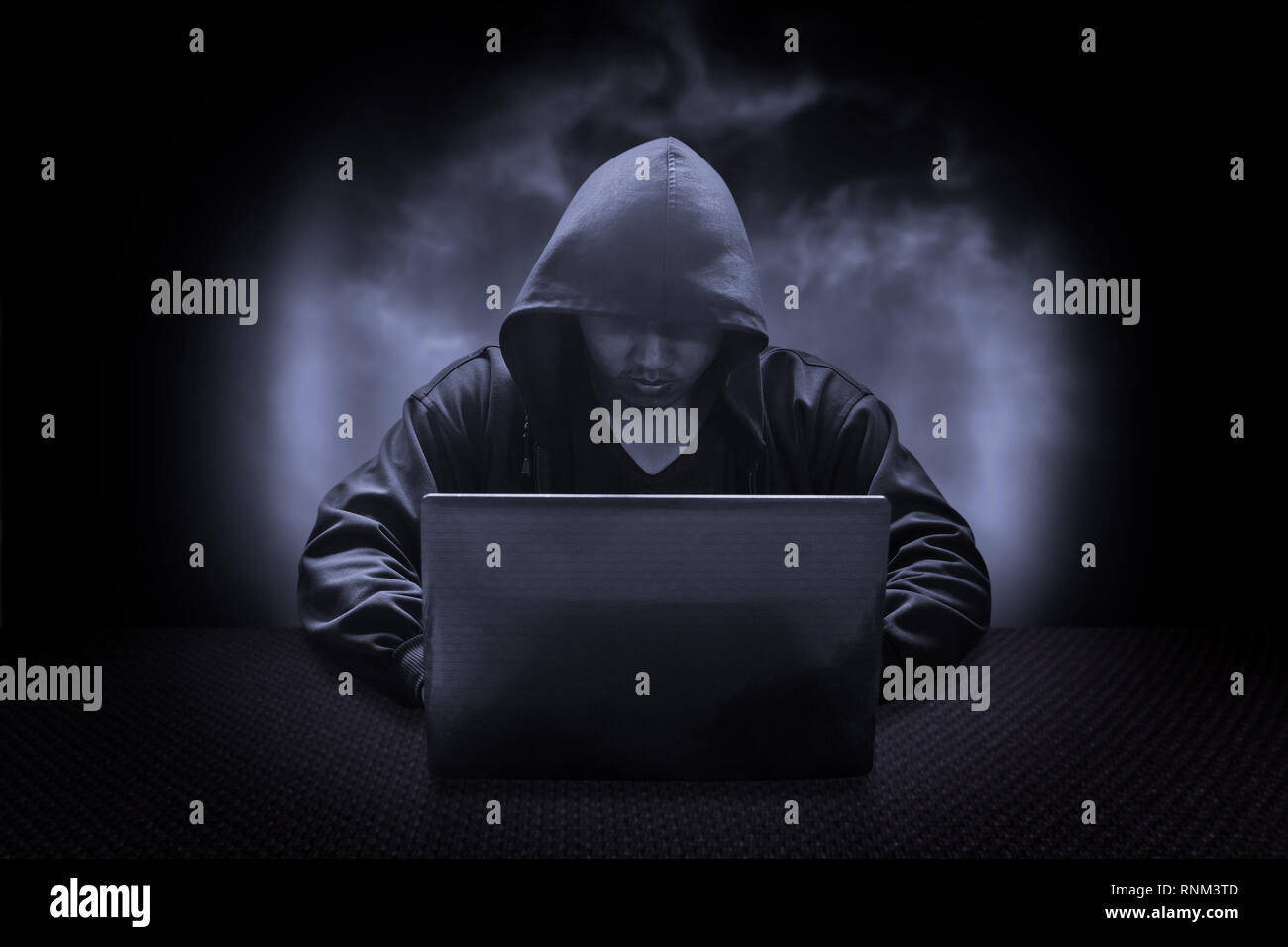 Hooded computer hacker stealing information with laptop Stock Photo