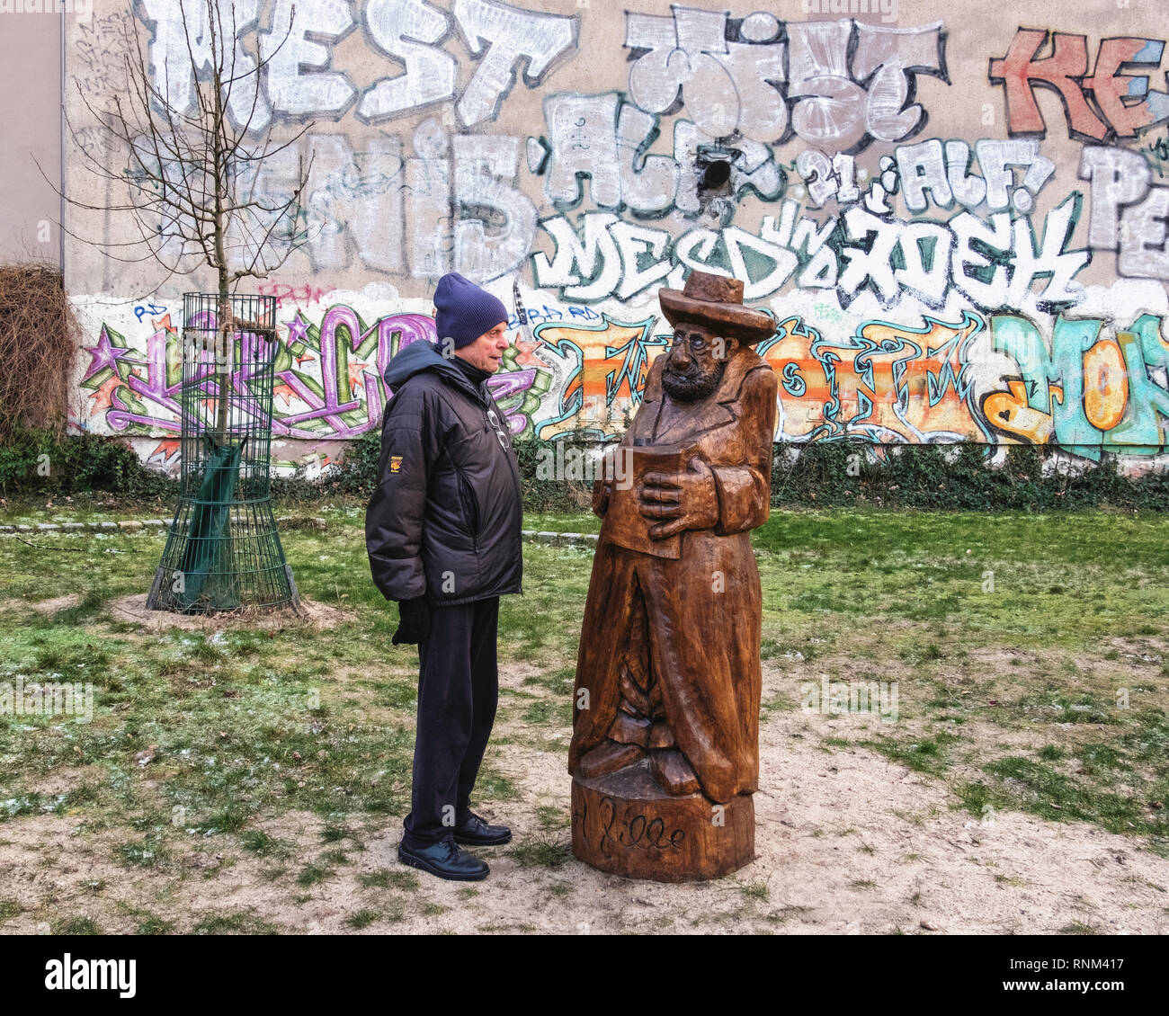 Berlin Mitte, Heinrich-Zille-Park, Elderly man and wooden sculpture of man with book in Children’s adventure playground in Bergstraße, Stock Photo