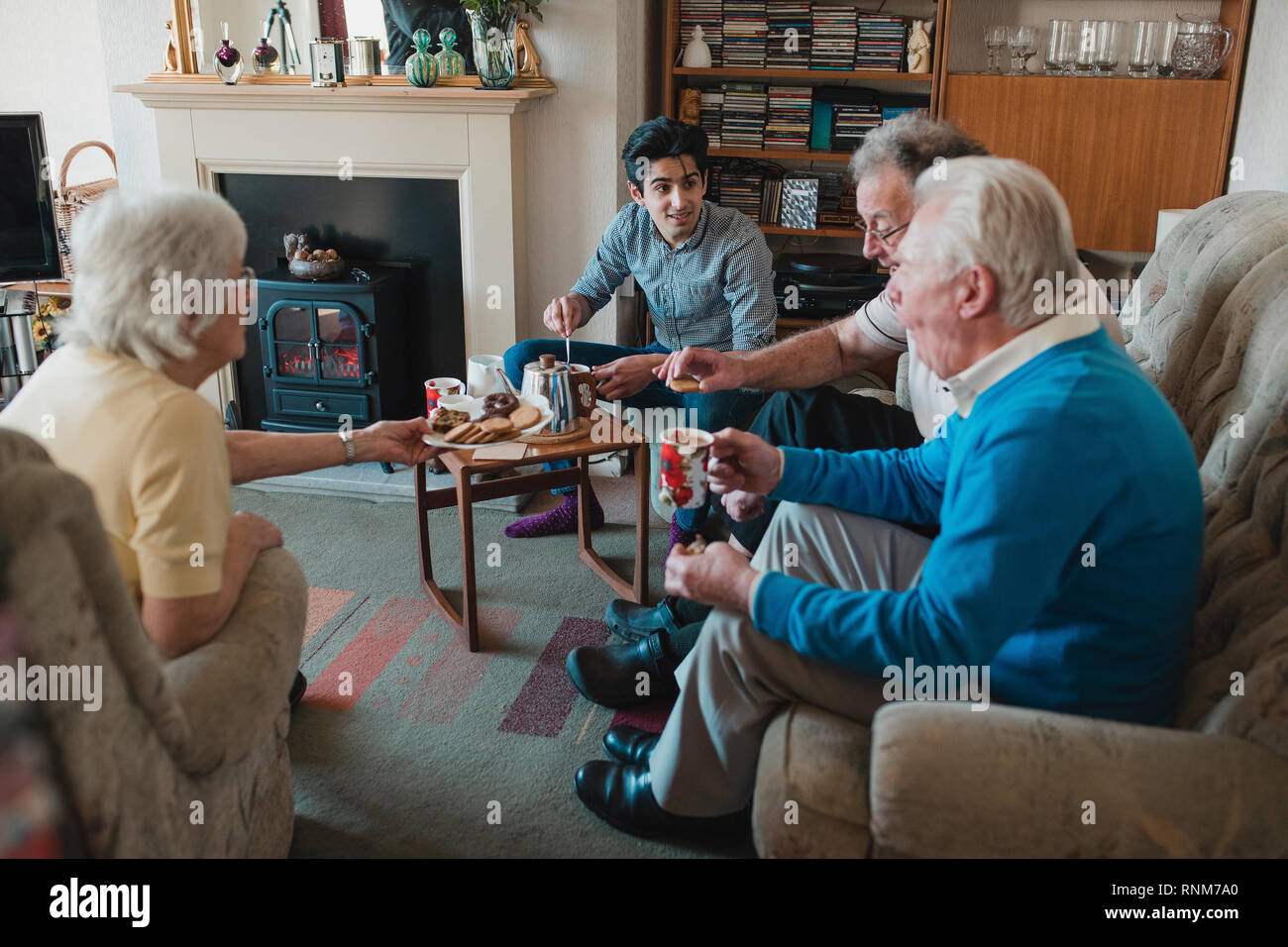 Teenage boy is assisting senior adults having a tea party at a nursing home. Stock Photo