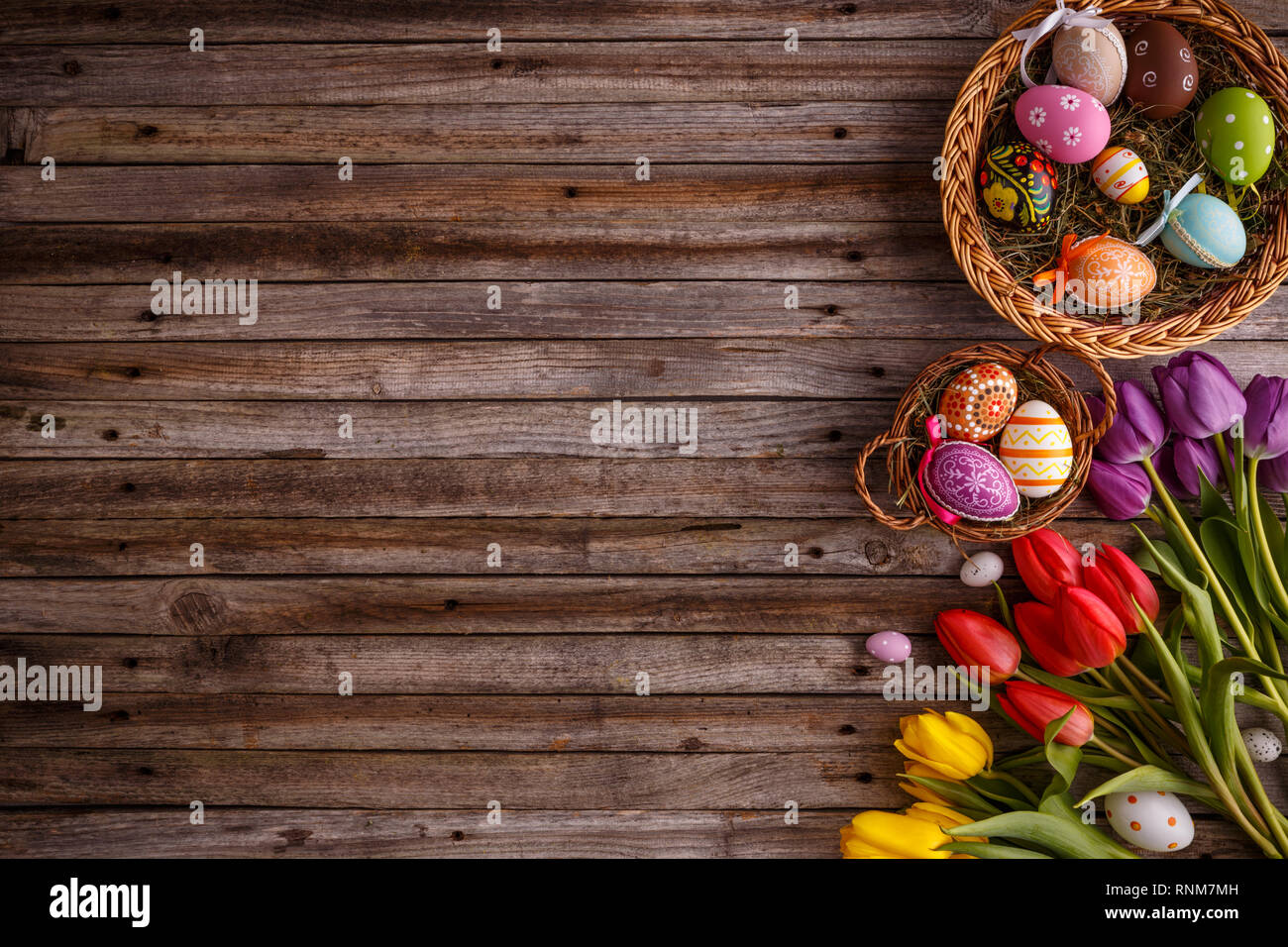 Colorful Easter eggs in basket and tulip flowers on wooden table Stock Photo