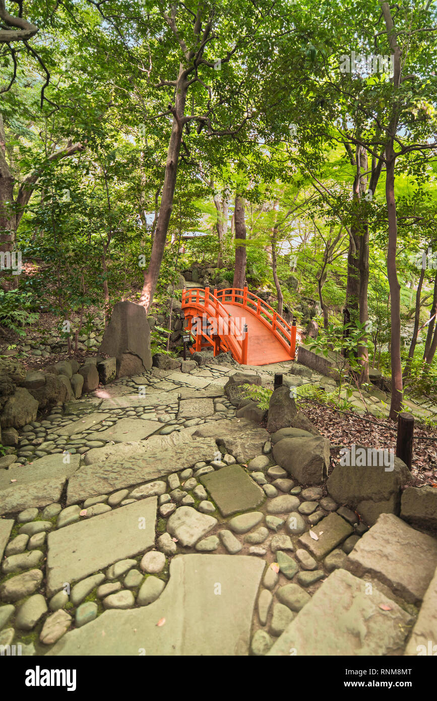 Spiral staircase paved with stones and pebbles leading to the Japanese vermilion Tsuten bridge surrounded by maples and cherry trees in the forest of  Stock Photo