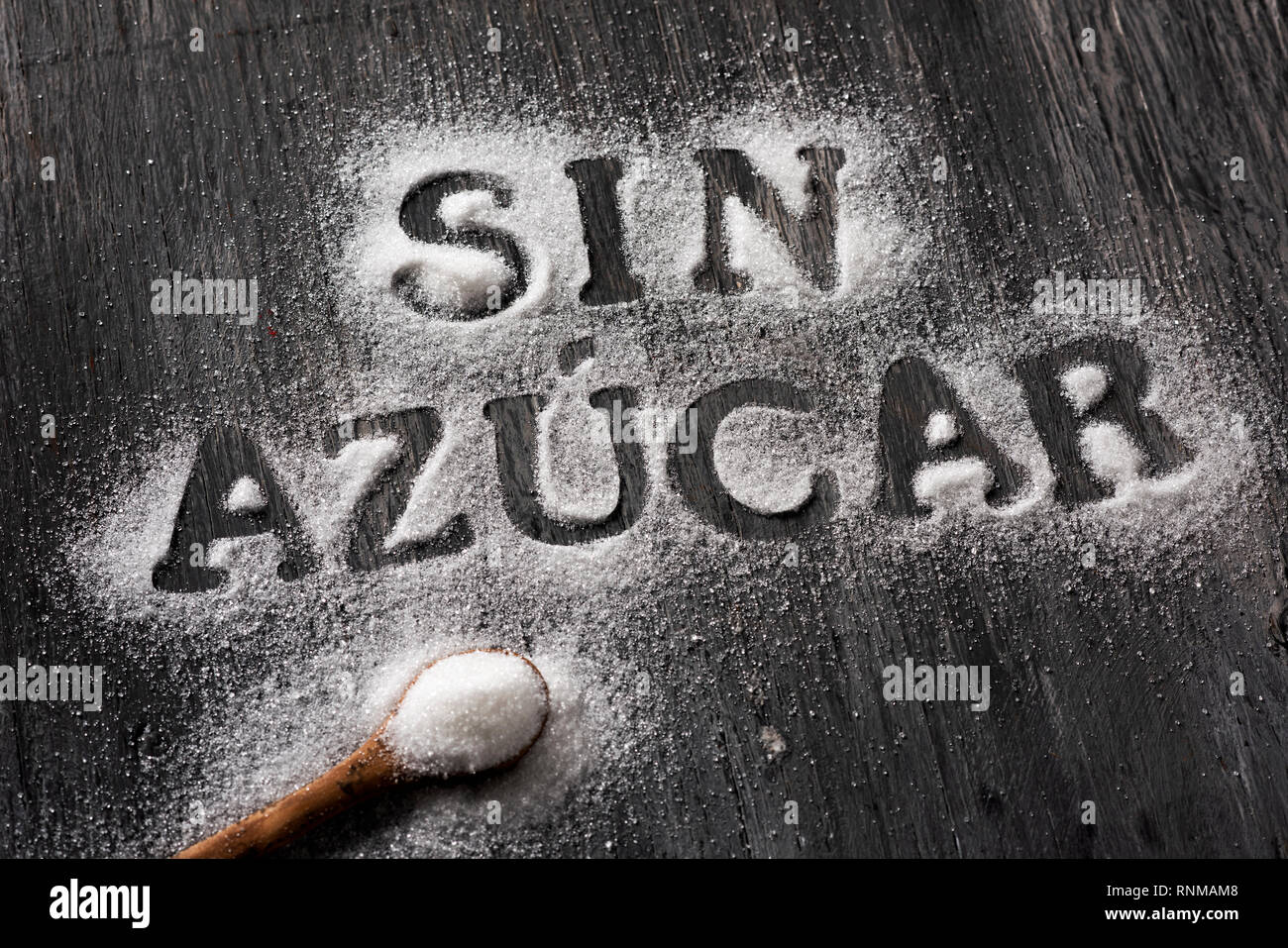 high angle view of a rustic gray wooden table sprinkled with sugar where you can read the text sin azucar, sugar free written in Spanish, and a spoon  Stock Photo
