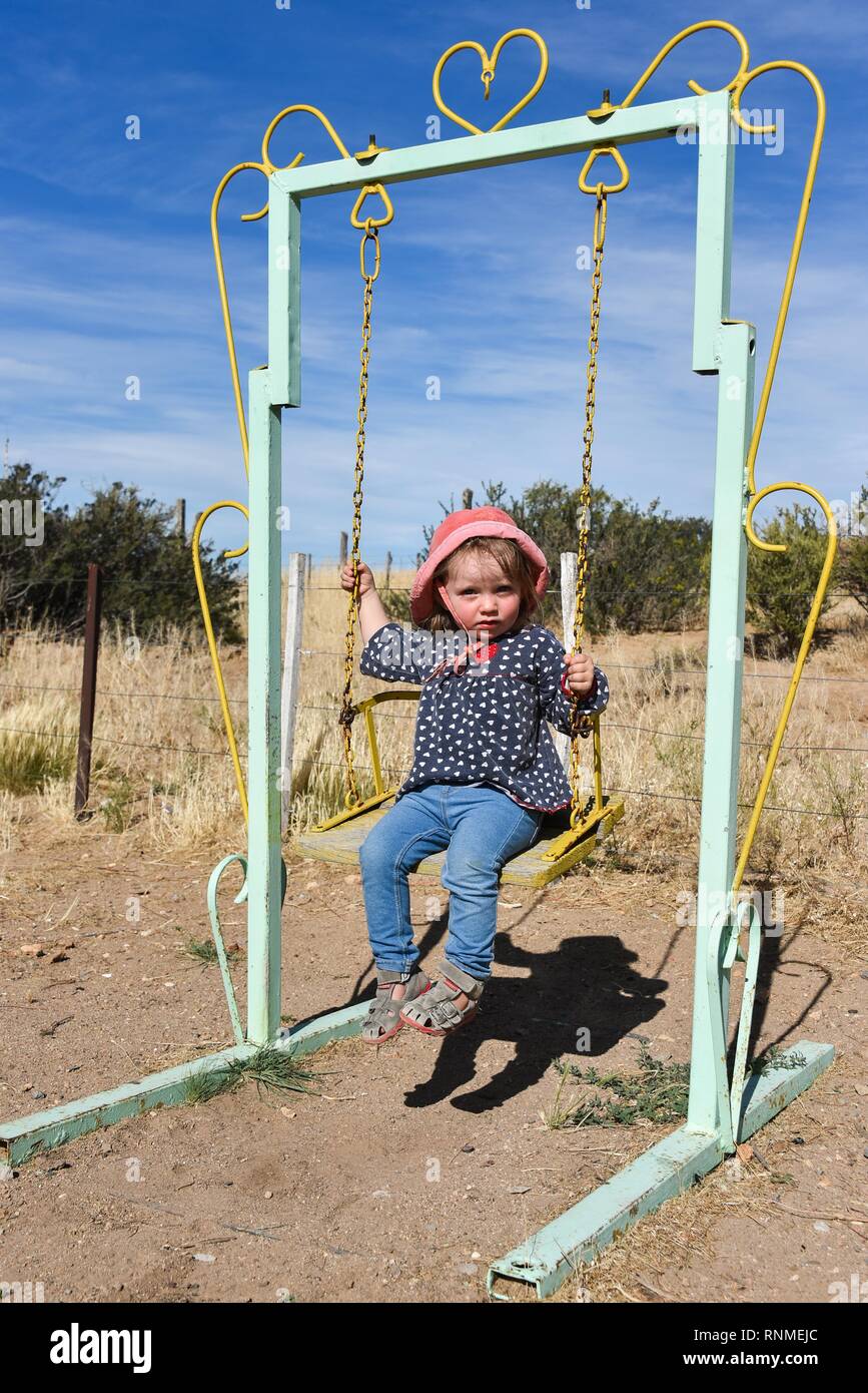 Little girl with red hat rocking on an old swing, Patagonia, Argentina Stock Photo