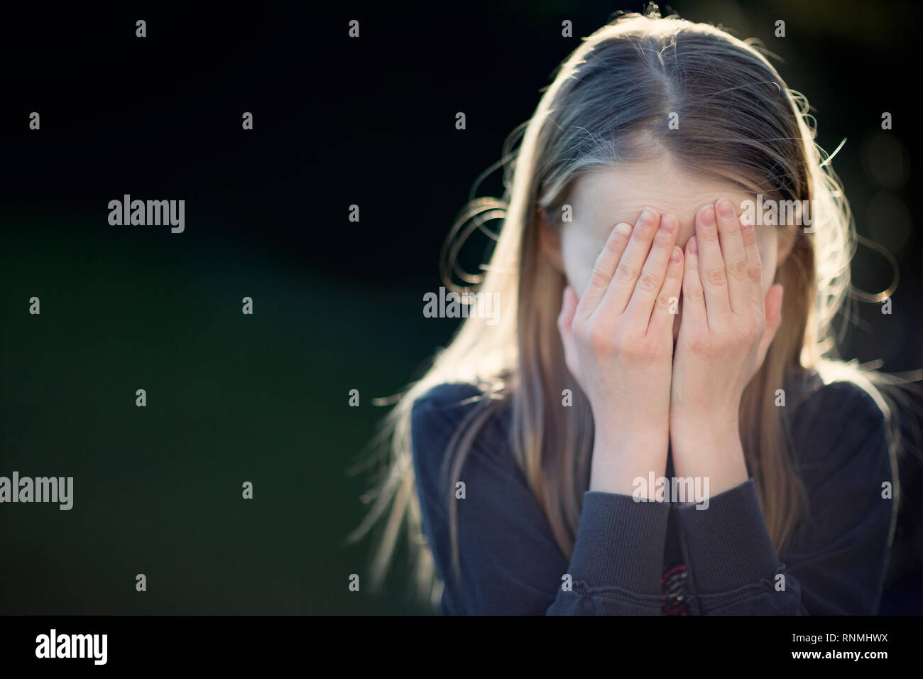 Child hiding her face behind her hands in despair Stock Photo