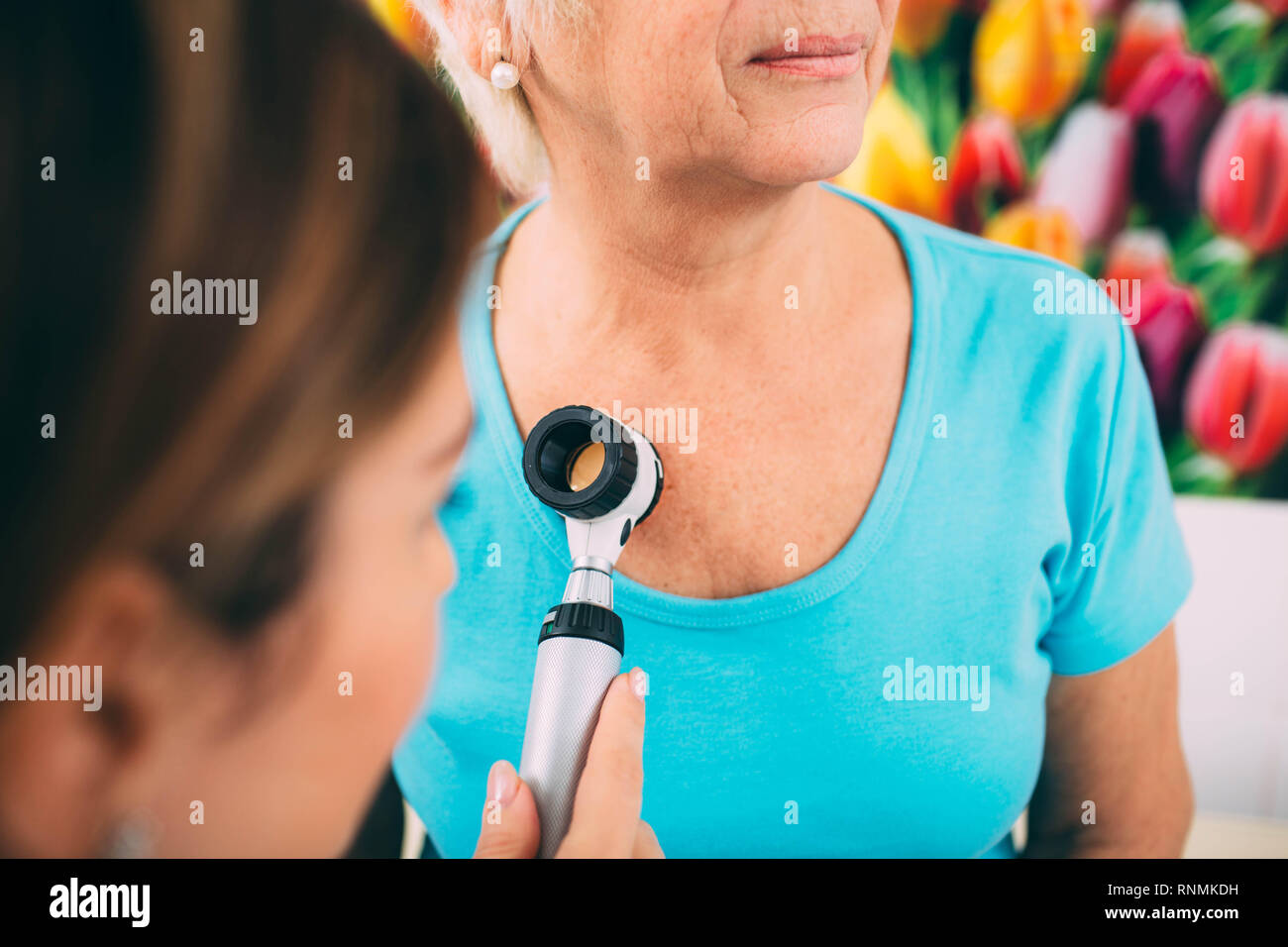 Doctor dermatologist examining her senior patient using dermatoscope. Stock Photo