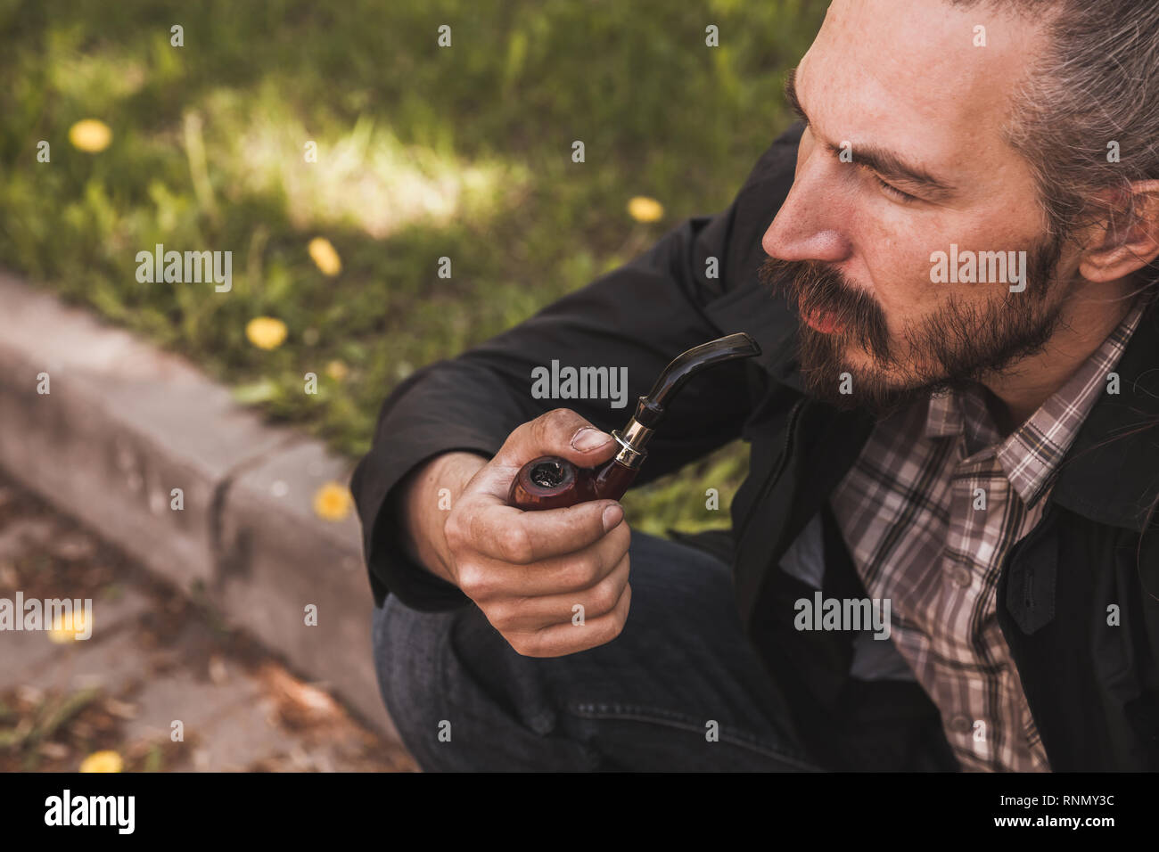 Bearded man smoking pipe in summer park, close up portrait Stock Photo