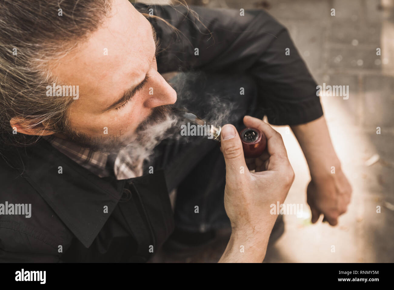 Bearded brutal man smoking pipe in park, close up portrait Stock Photo