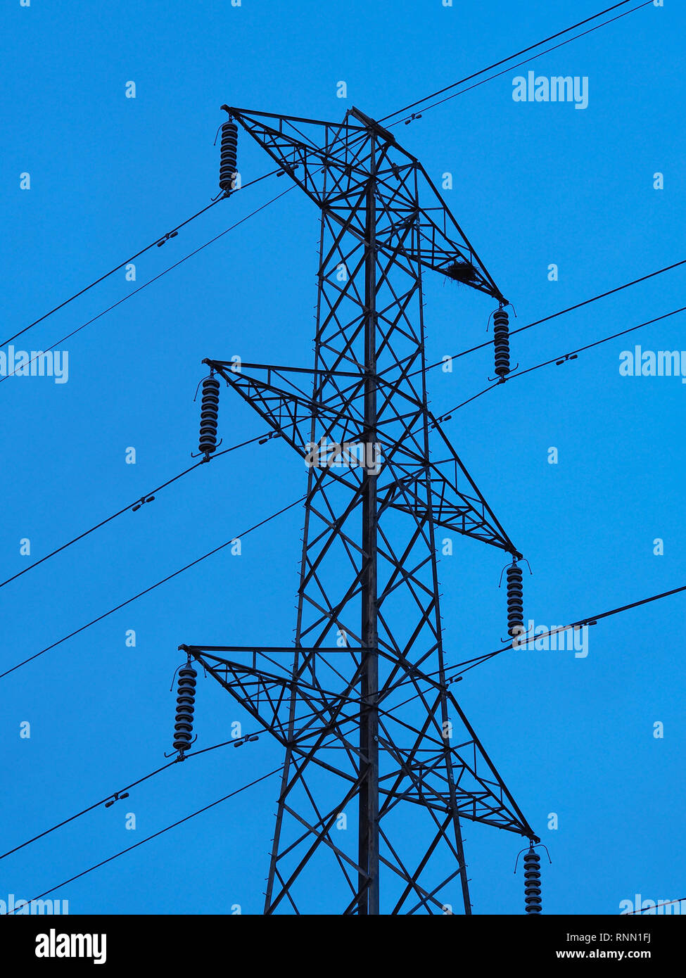 Tall metal pylon supporting power lines with a clear blue sky background Stock Photo