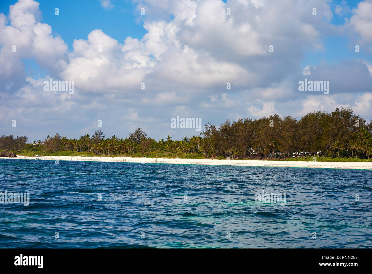 View of coastline with beach in Kenya, Africa. People, tourists on vacation and sea with waves and surf, under a blue sky with clouds. Stock Photo