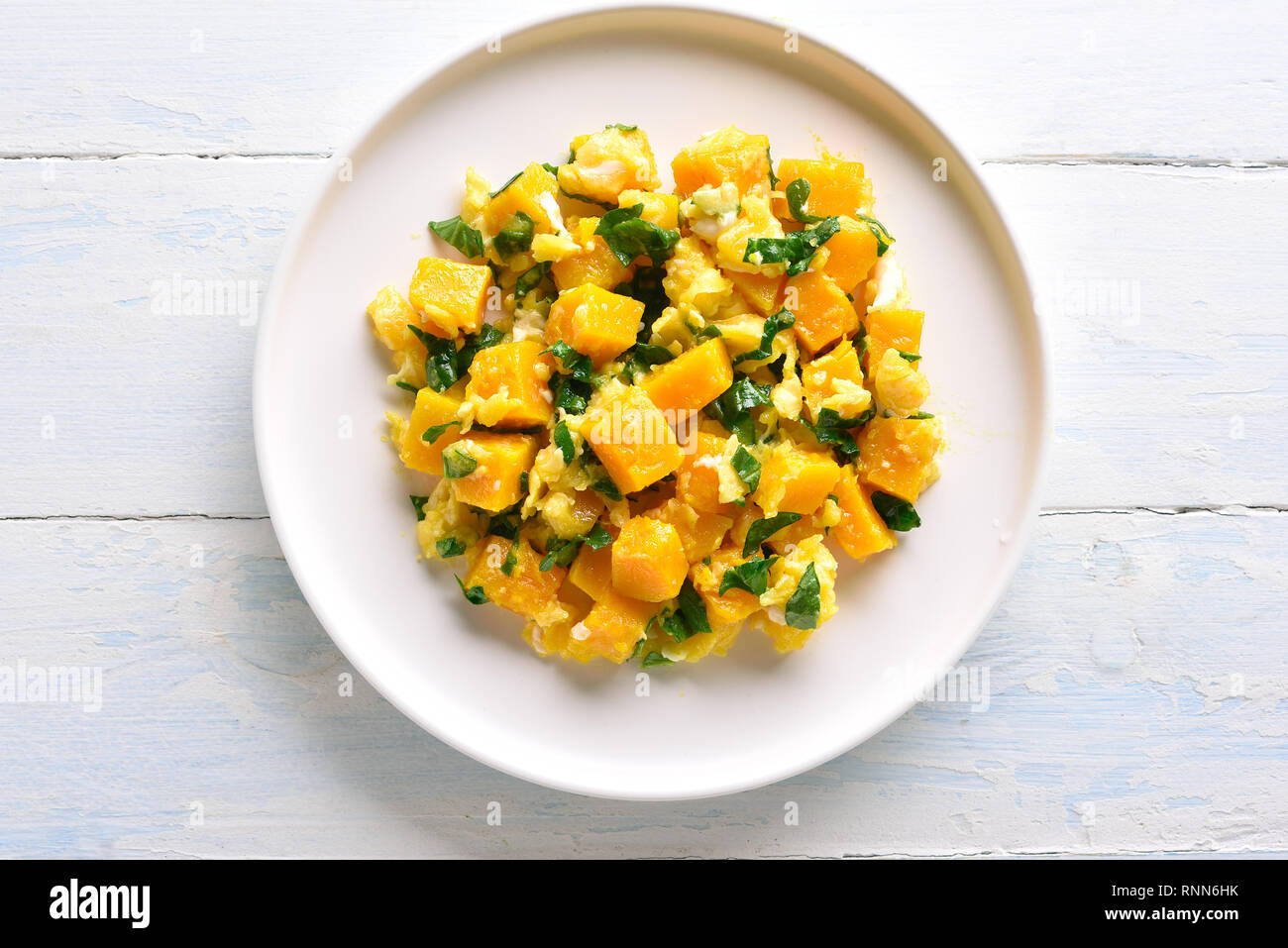 Stirfried pumpkin with eggs on plate over white wooden background. Pumpkin and egg stir fry in