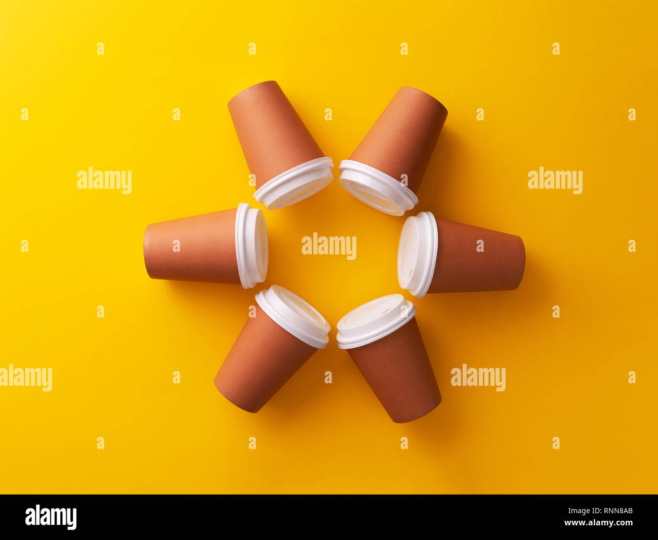 Multiple disposable coffee cups organized in a circle over yellow