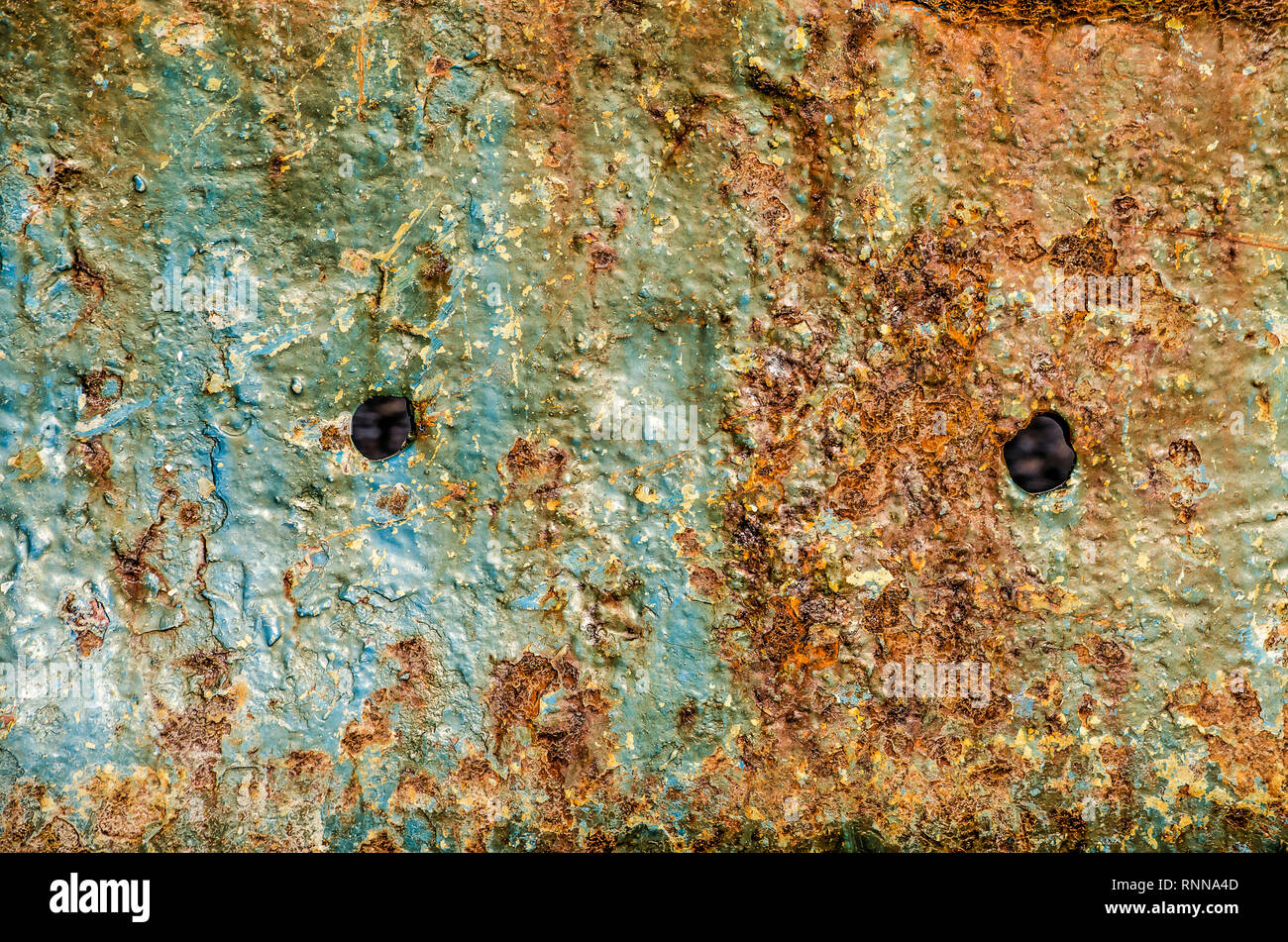 Detail of a ship hull with two small holes and brown patches of rust eating away the light blue paint Stock Photo