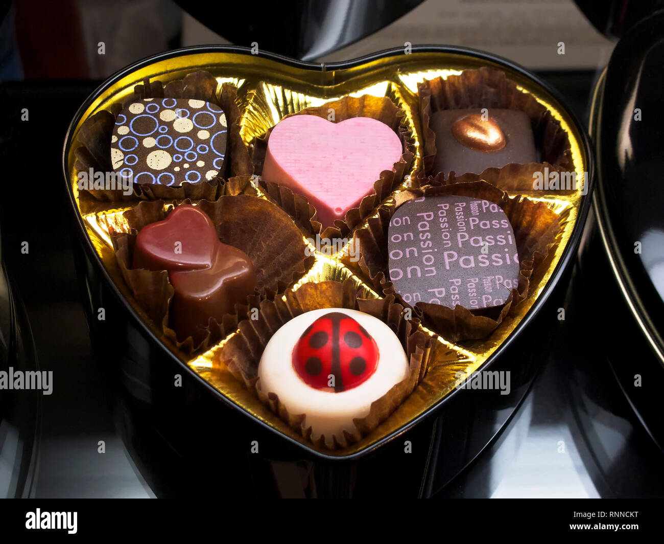 Six different kind of pralines in an open heartshaped golden metal box