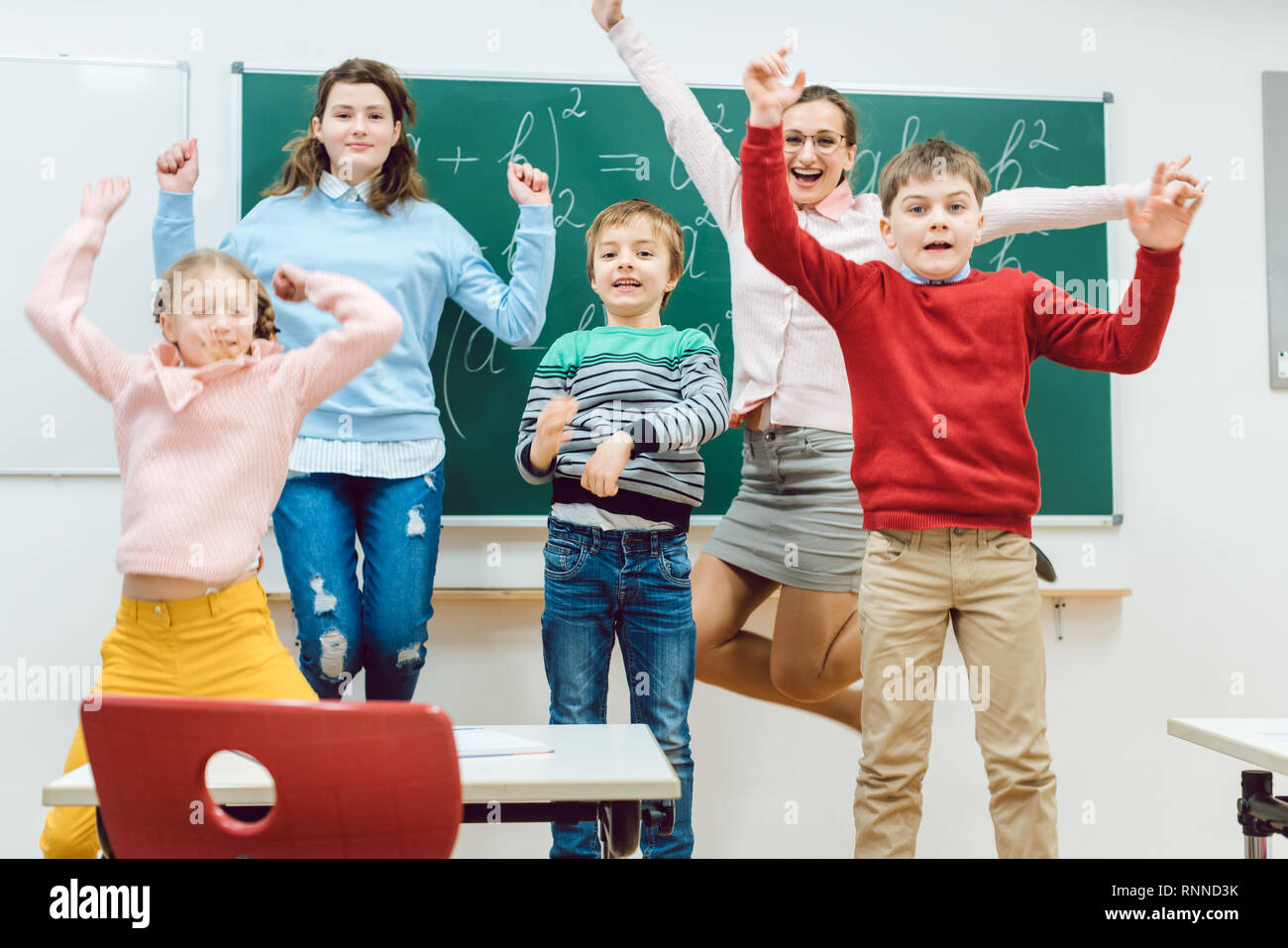 Teacher and students of primary school jumping in classroom Stock Photo Alamy