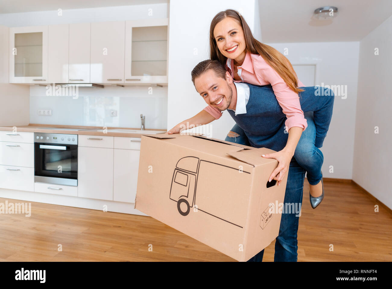 Man carrying his wife and a moving box into the new apartment Stock Photo