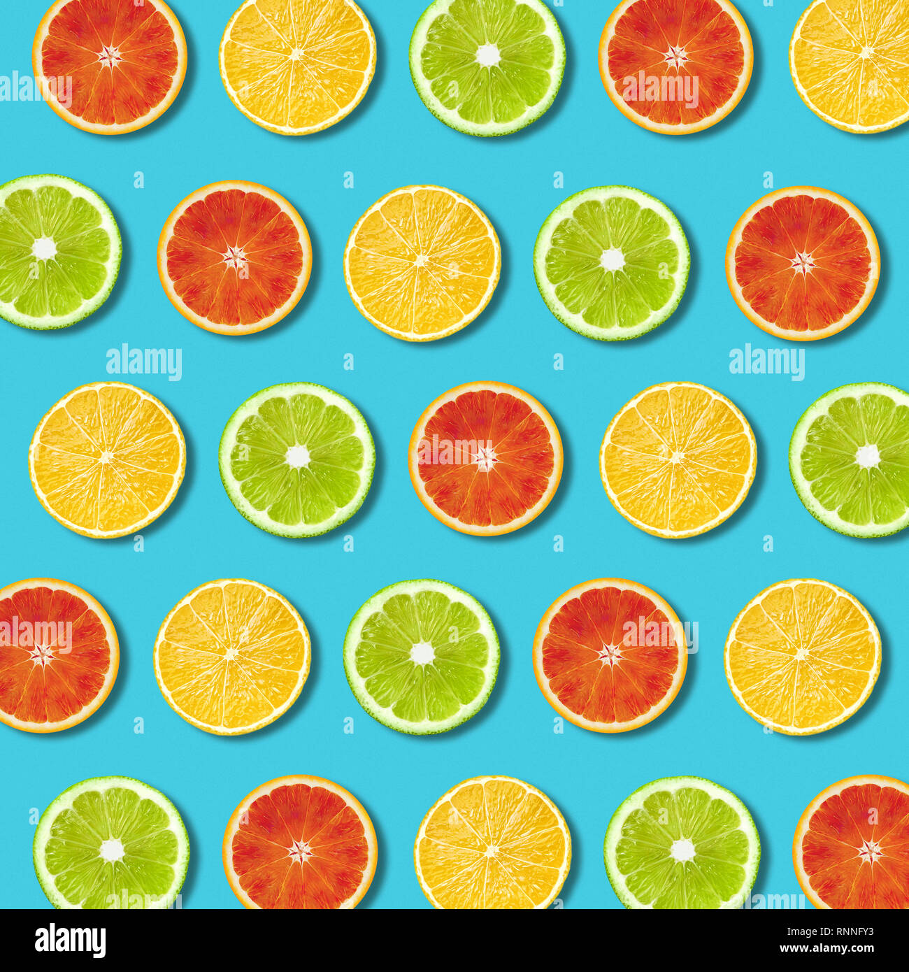 Multicolored vibrant lemon, green lime and red orande slices pattern on turquoise background. Minimal flat lay top view food texture Stock Photo