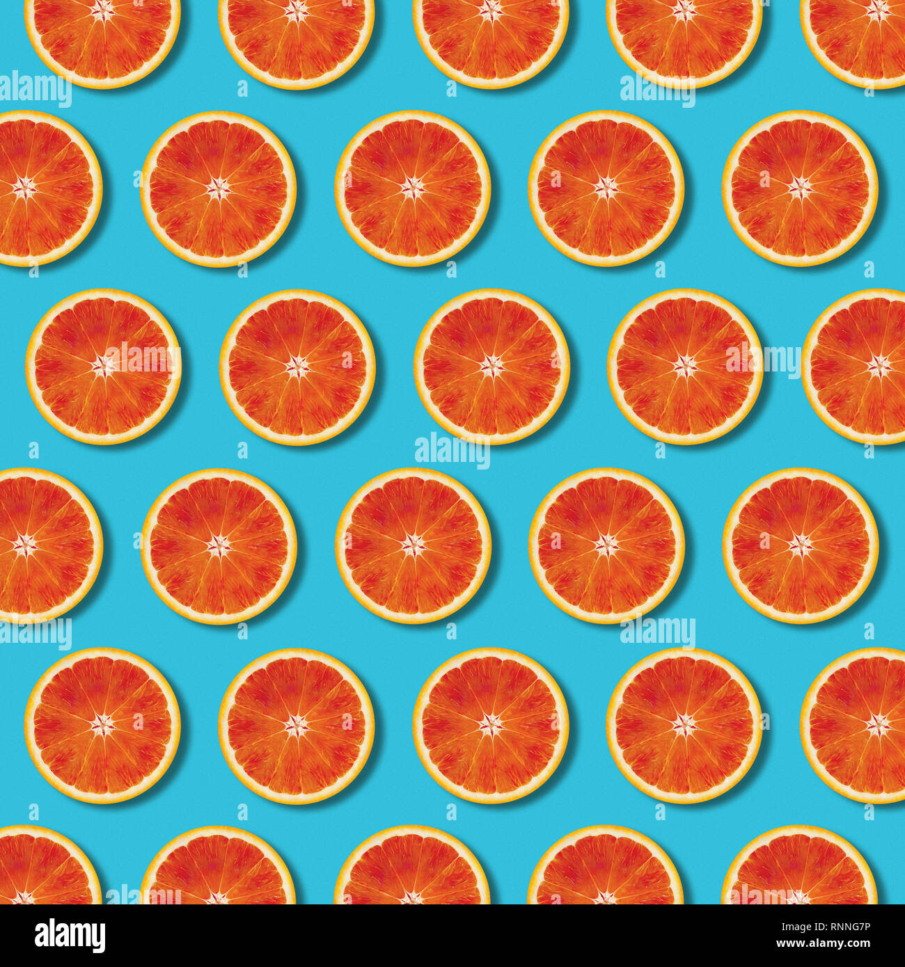 Red orange slices pattern on vibrant turquoise color background. Minimal flat lay top view food texture Stock Photo