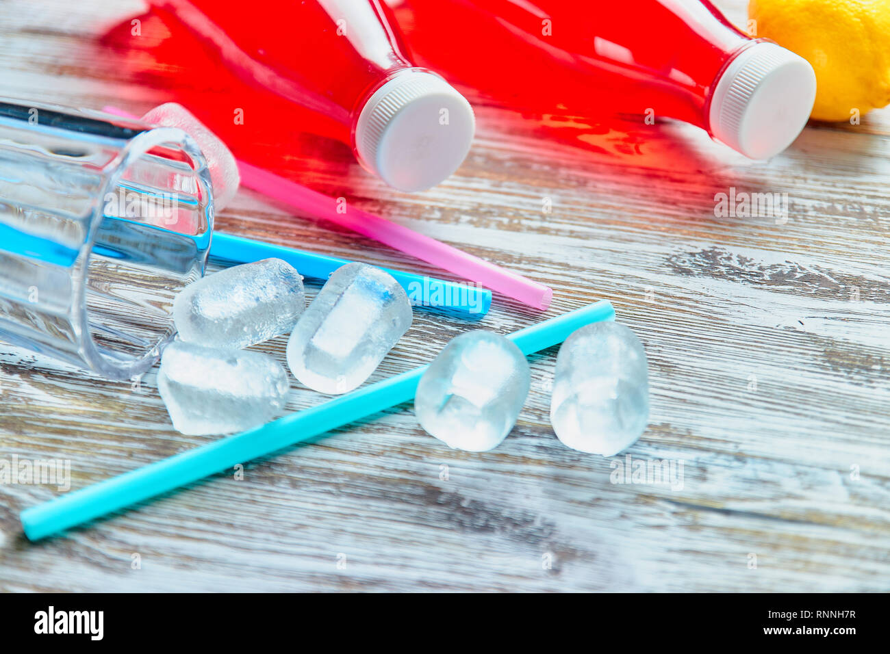 plastic bottles with berries, refreshing drink. scattered ice cubes and drinking straws. on the background of a shabby wooden table. close up. copy Stock Photo