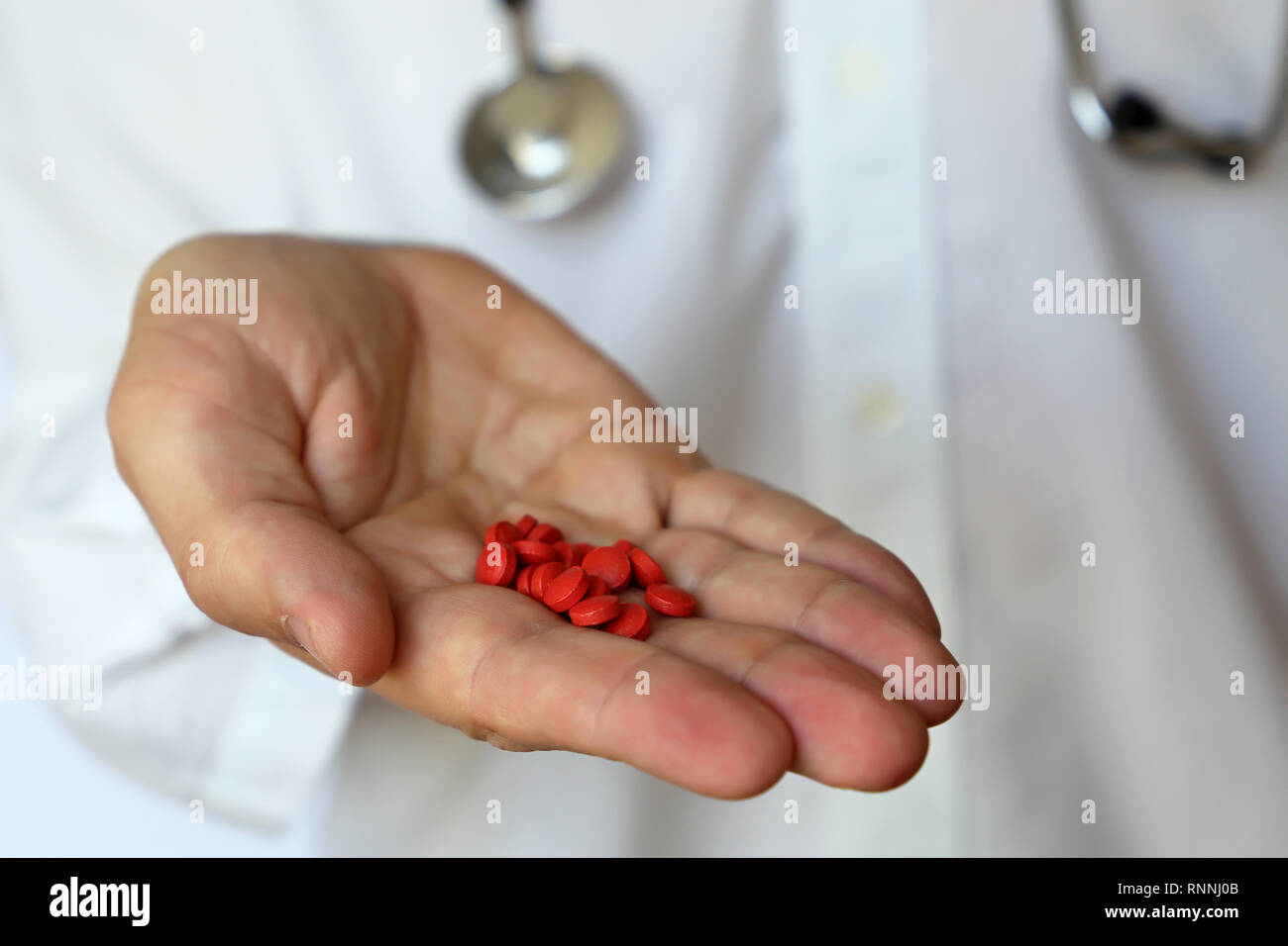 Doctor with red pills, man with stethoscope giving medication in capsules. Concept of medical prescription, dose of drugs, vitamins, pharmacy Stock Photo