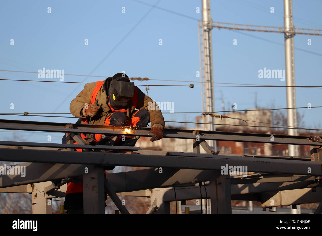 Welder working on scaffolding in the city. Construction worker against the clear blue sky background, welding works Stock Photo
