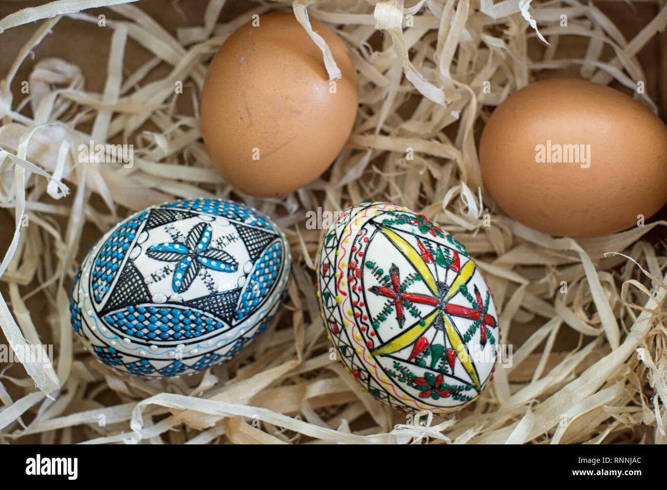 Two decorated easter eggs and two fresh organic eggs on straw Stock Photo