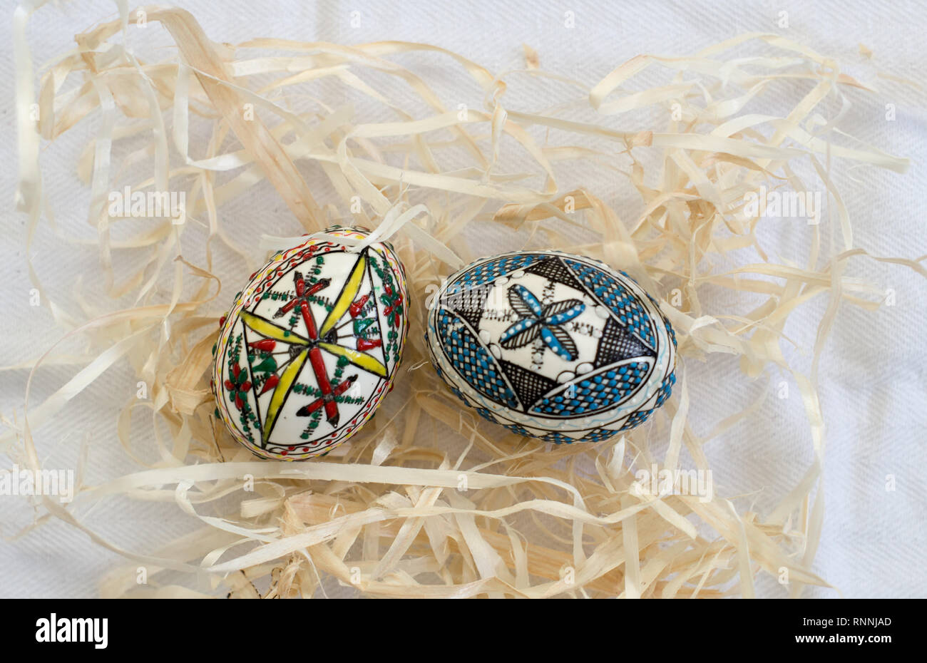 Two traditional handmade  Easter eggs in straw on white cloth. Traditional pattern from Bucovina Stock Photo
