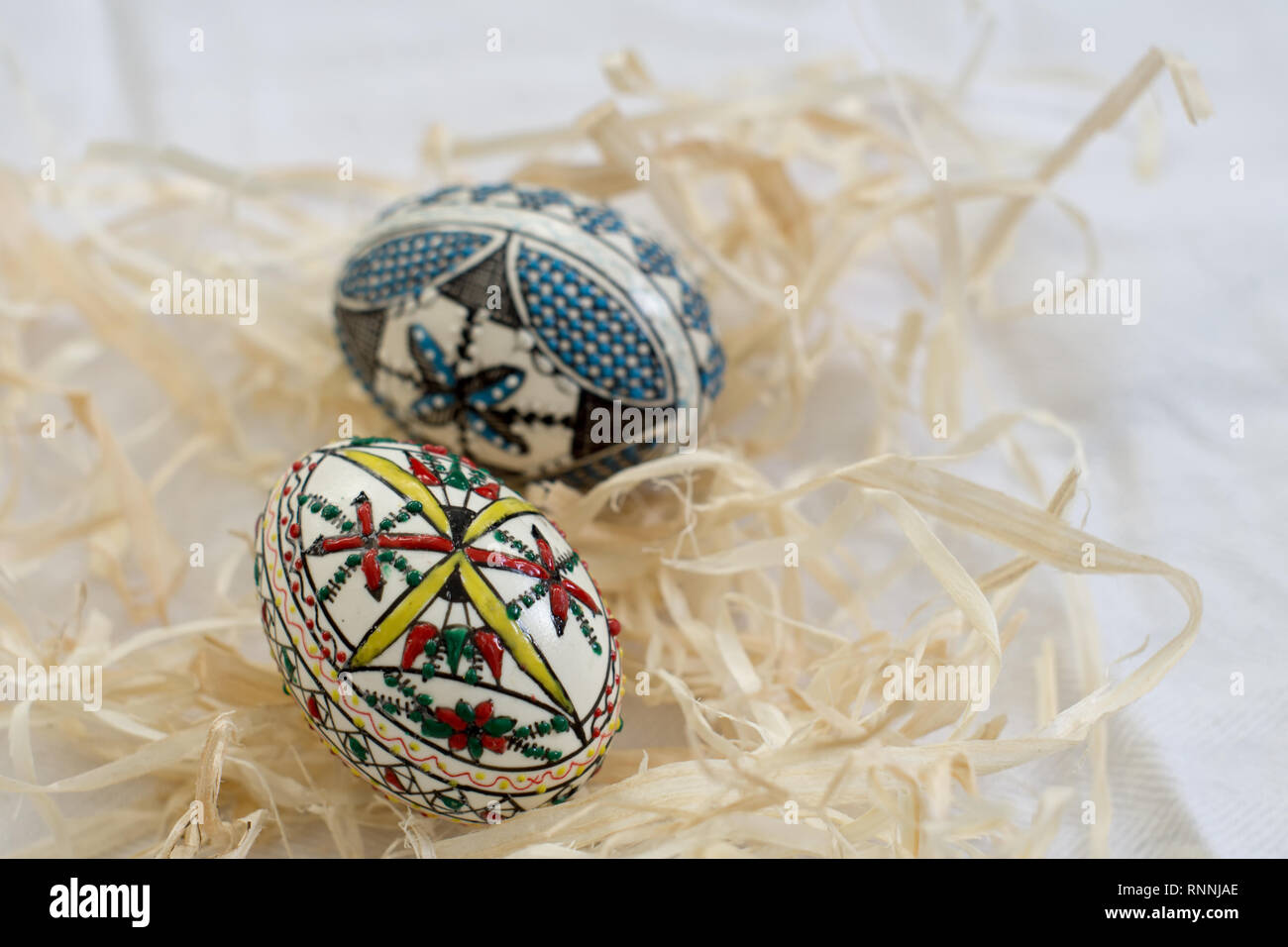 Two traditional handmade  Easter eggs in straw on white cloth. Traditional pattern from Bucovina Stock Photo