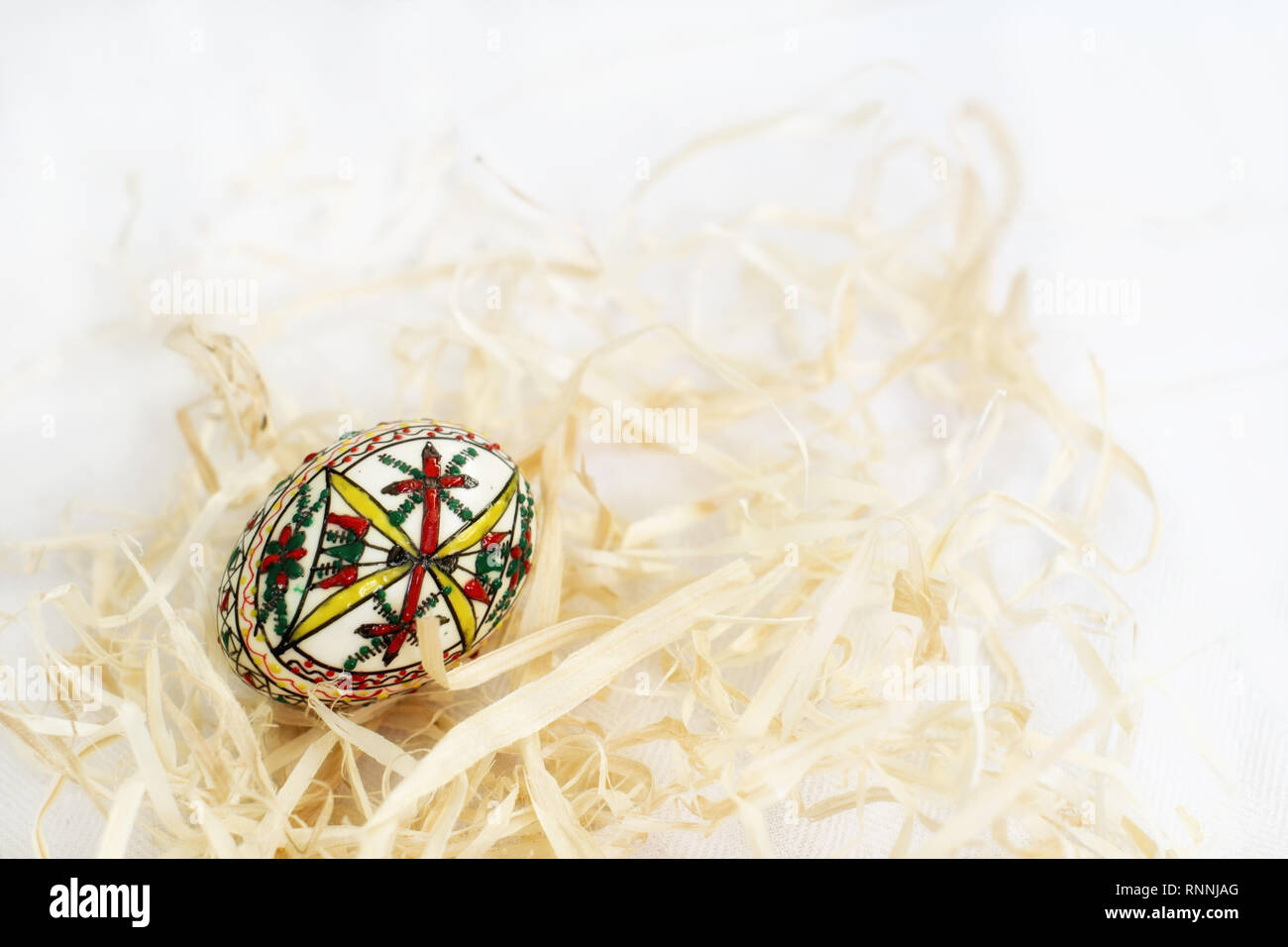 Traditional handmade  Easter egg in straw on white cloth. Traditional pattern from Bucovina Stock Photo