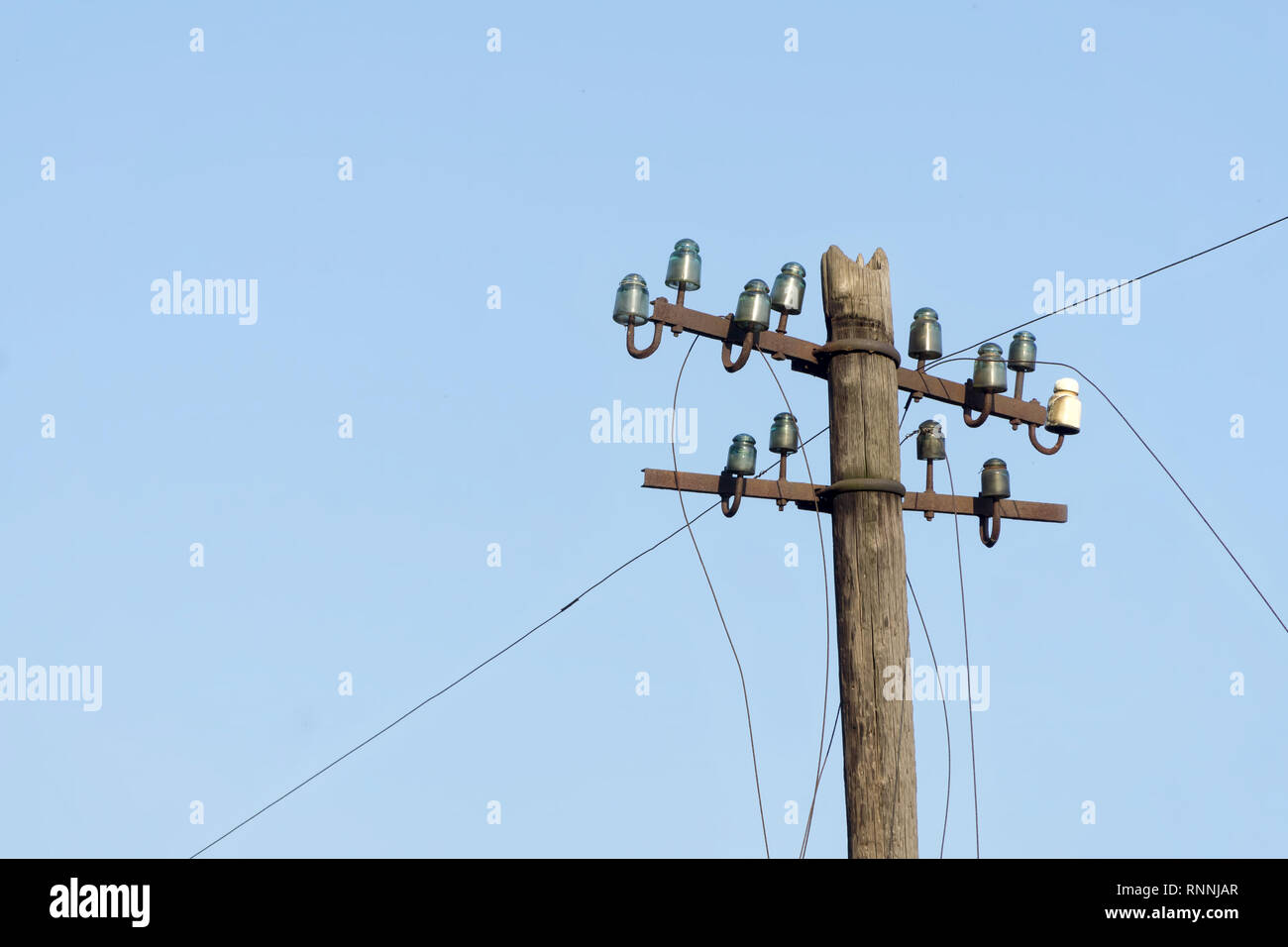 Old electric  wooden pole with glass and ceramic insulators and electric wires against blue sky. Copy space. Stock Photo