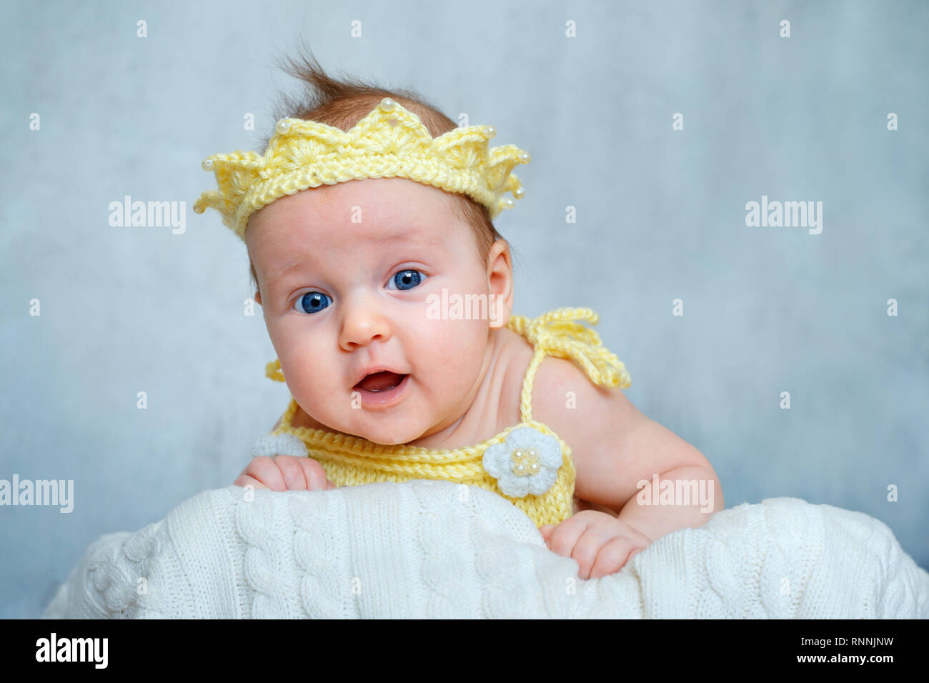 Portrait of a cute newborn baby girl in yellow knitted crown lying on her stomach Stock Photo