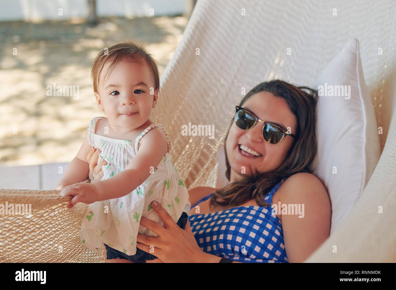 Baby girl with mom laying on beach in hammock Stock Photo