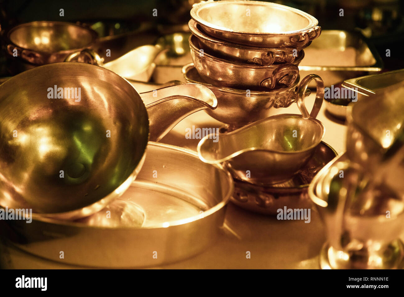 Heavy silver bowls and sauce bowls stacked in golden light. Stock Photo
