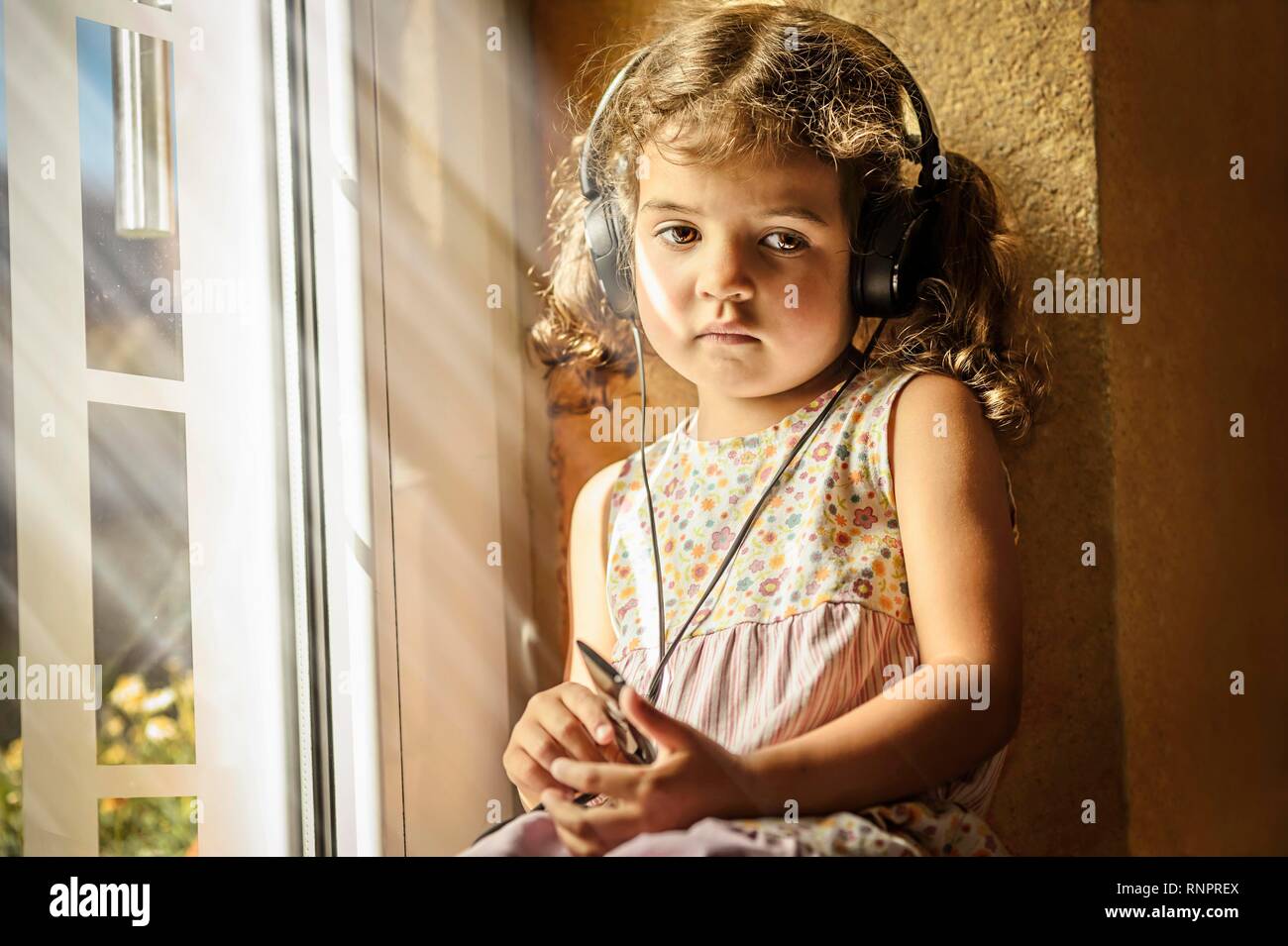 Girl, 3 years old, listens to thoughtful music with headphones, Germany Stock Photo