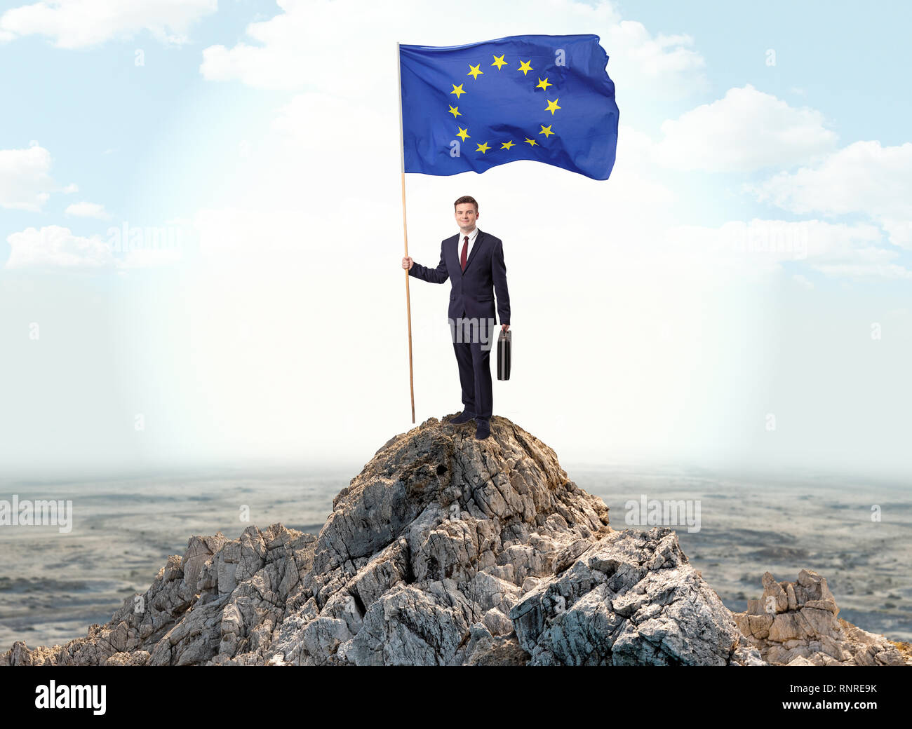 Successful businessman on the top of a mountain holding victory flag ...