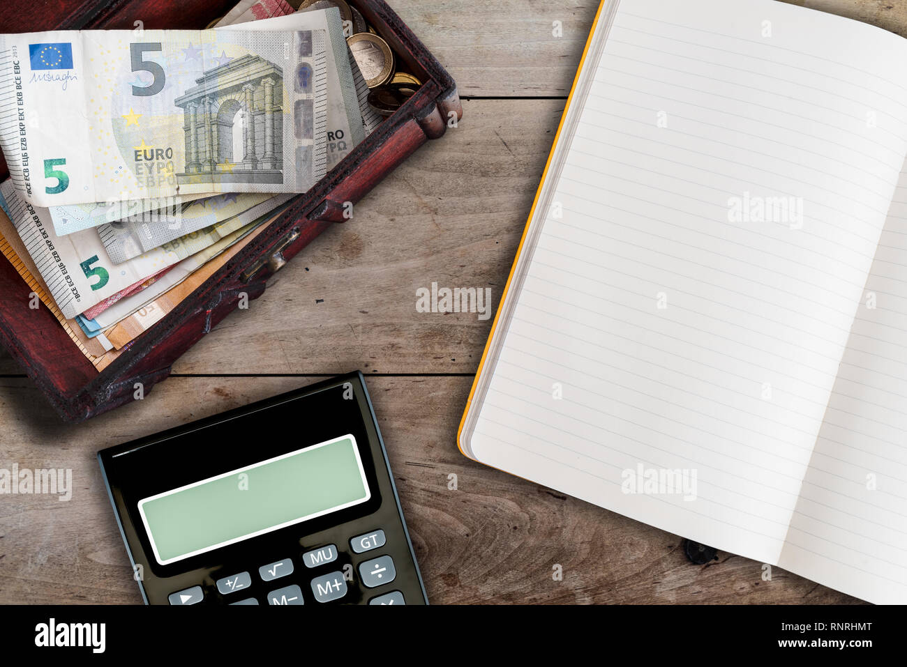 finance and housekeeping concept with open blank book, calculator and wooden box filled with cash on table Stock Photo