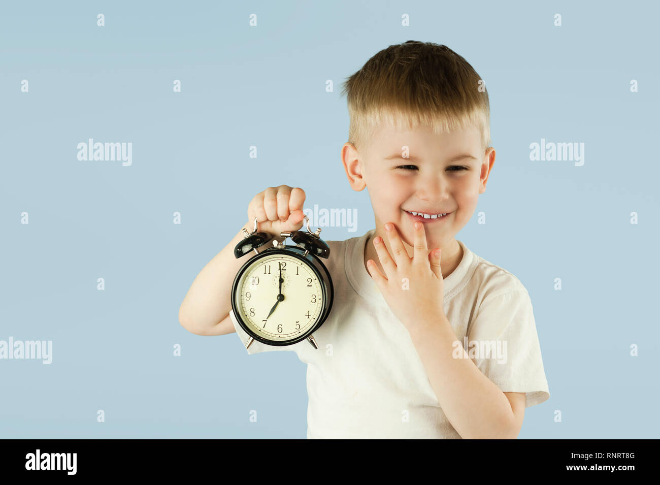 a beautiful child boy with an alarm clock in his hands early in the morning ziva and does not want to wake up on a Stock Photo