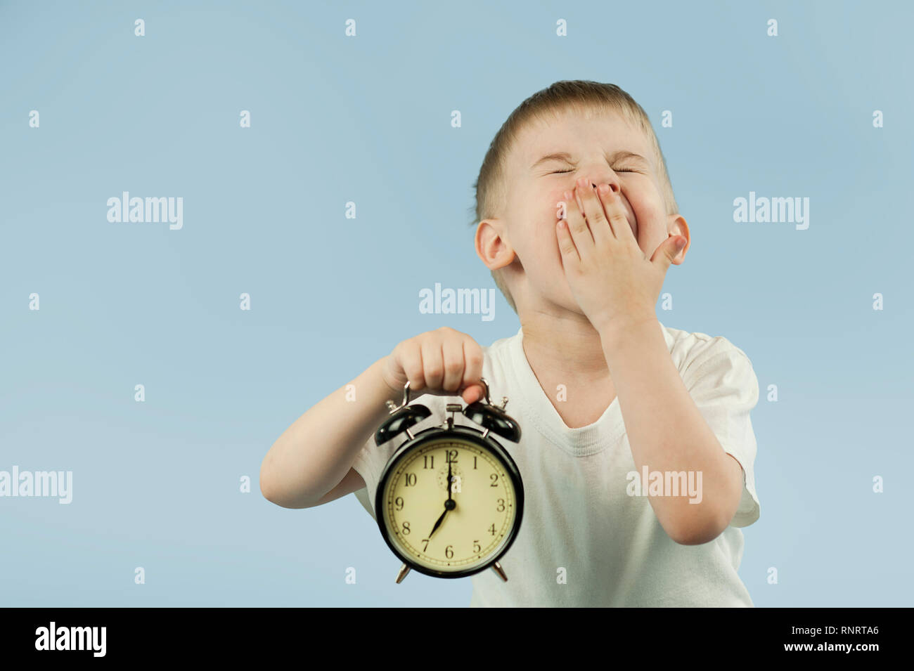 a beautiful child boy with an alarm clock in his hands early in the morning ziva and does not want to wake up on a Stock Photo