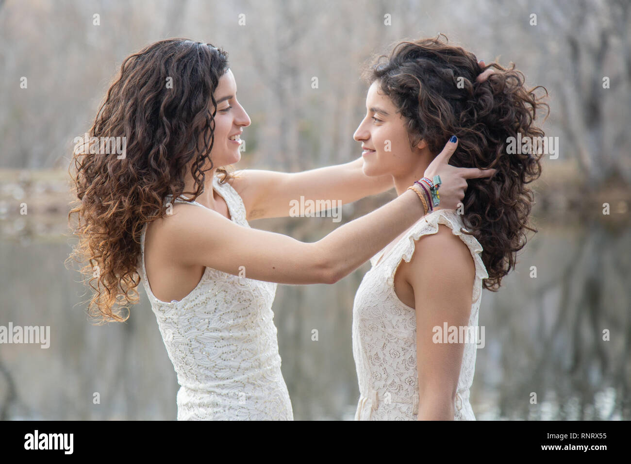 Side view of cheerful twin sisters standing at calm lake smiling and ...