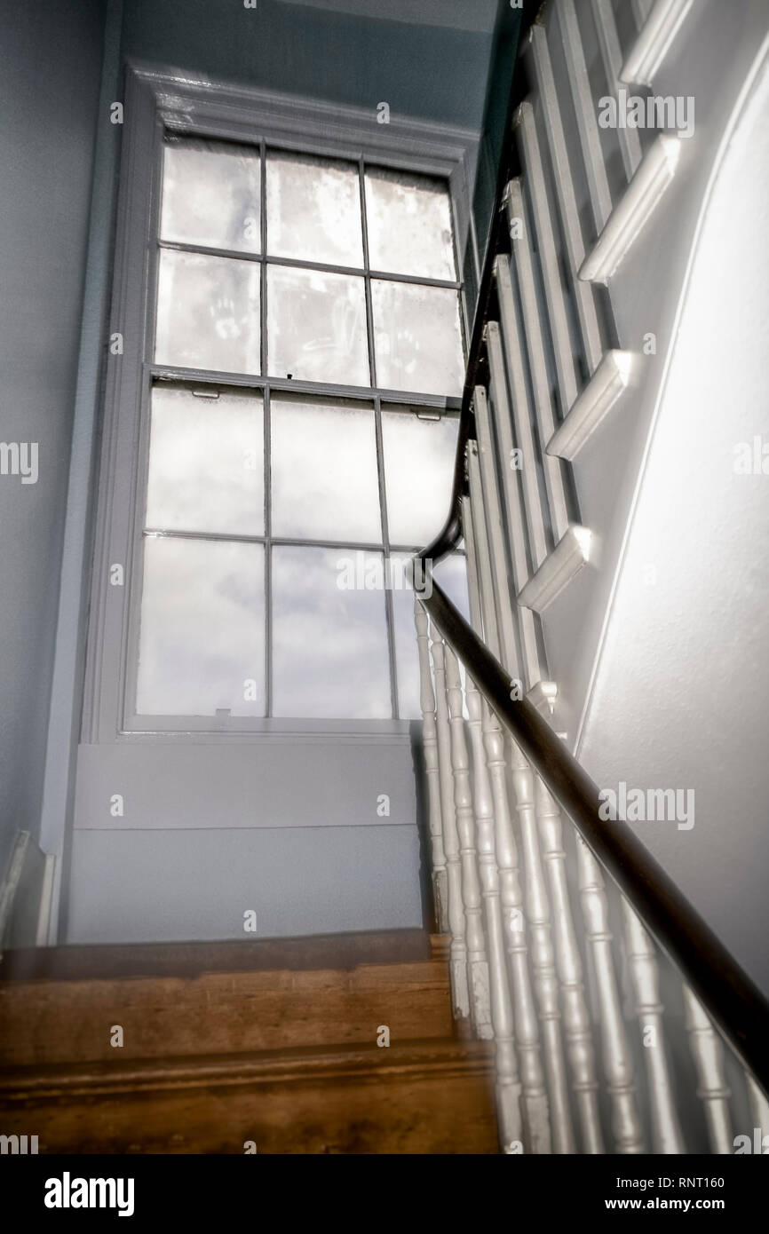 Hazy image of a large, grubby sash window on the half-landing of the stairway in a Victorian house Stock Photo