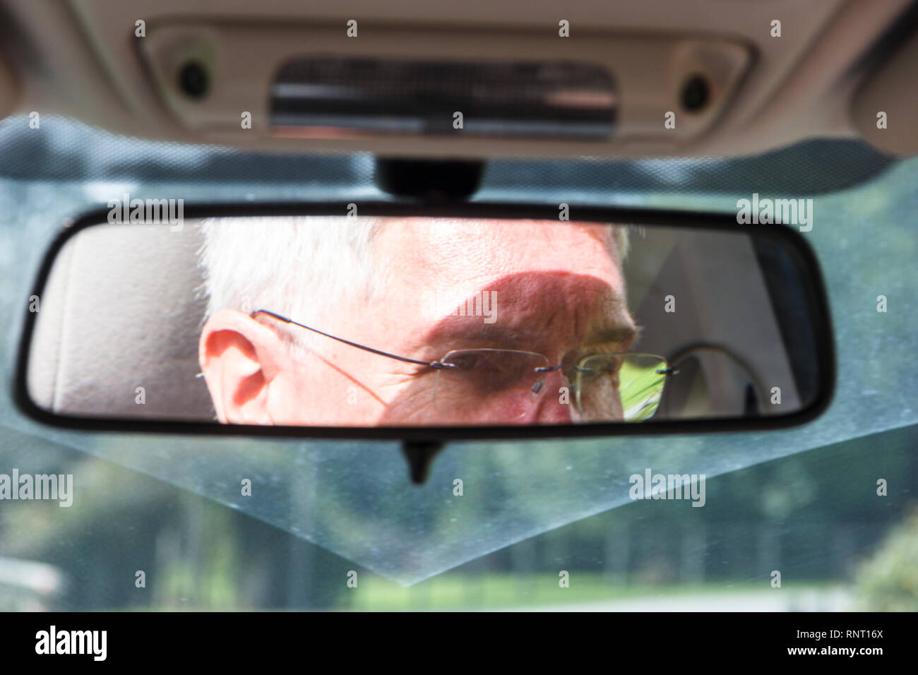 Reflection of an older male driver's head and eyes in the rear view mirror a a car Stock Photo