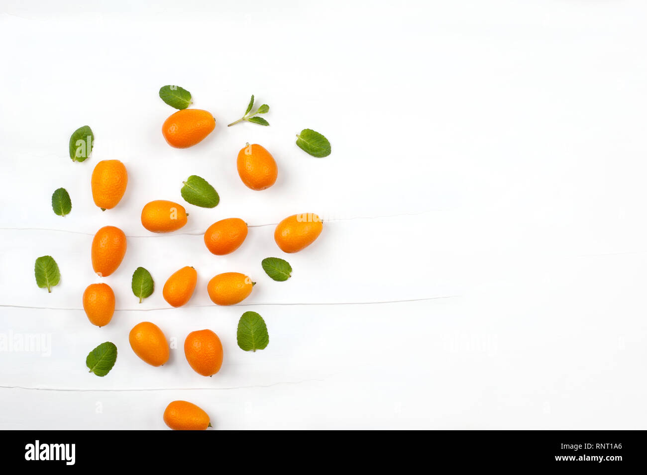 Creative background made with kumquat  fruits and mint  leafs.Kumquats whole, still life pattern background. Image with copy space. Stock Photo